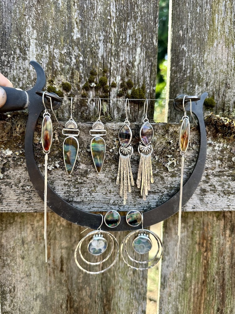Jewelry displayed on a black crescent-shaped stand against a weathered wooden background, including earrings, necklaces, and rings.