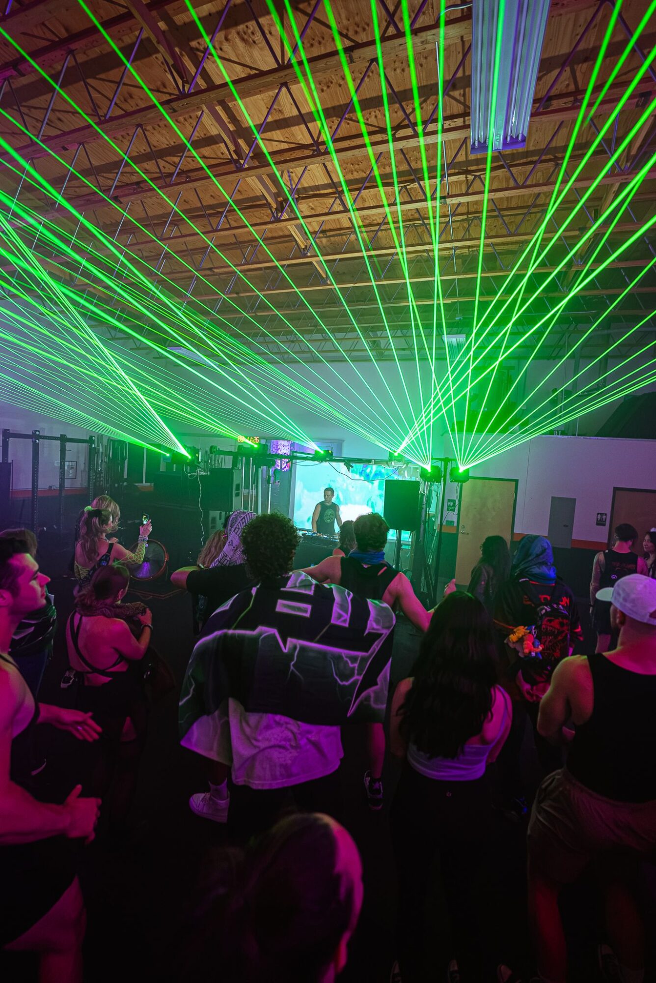 Crowd watching a laser light show with green and blue beams in a dark indoor venue.