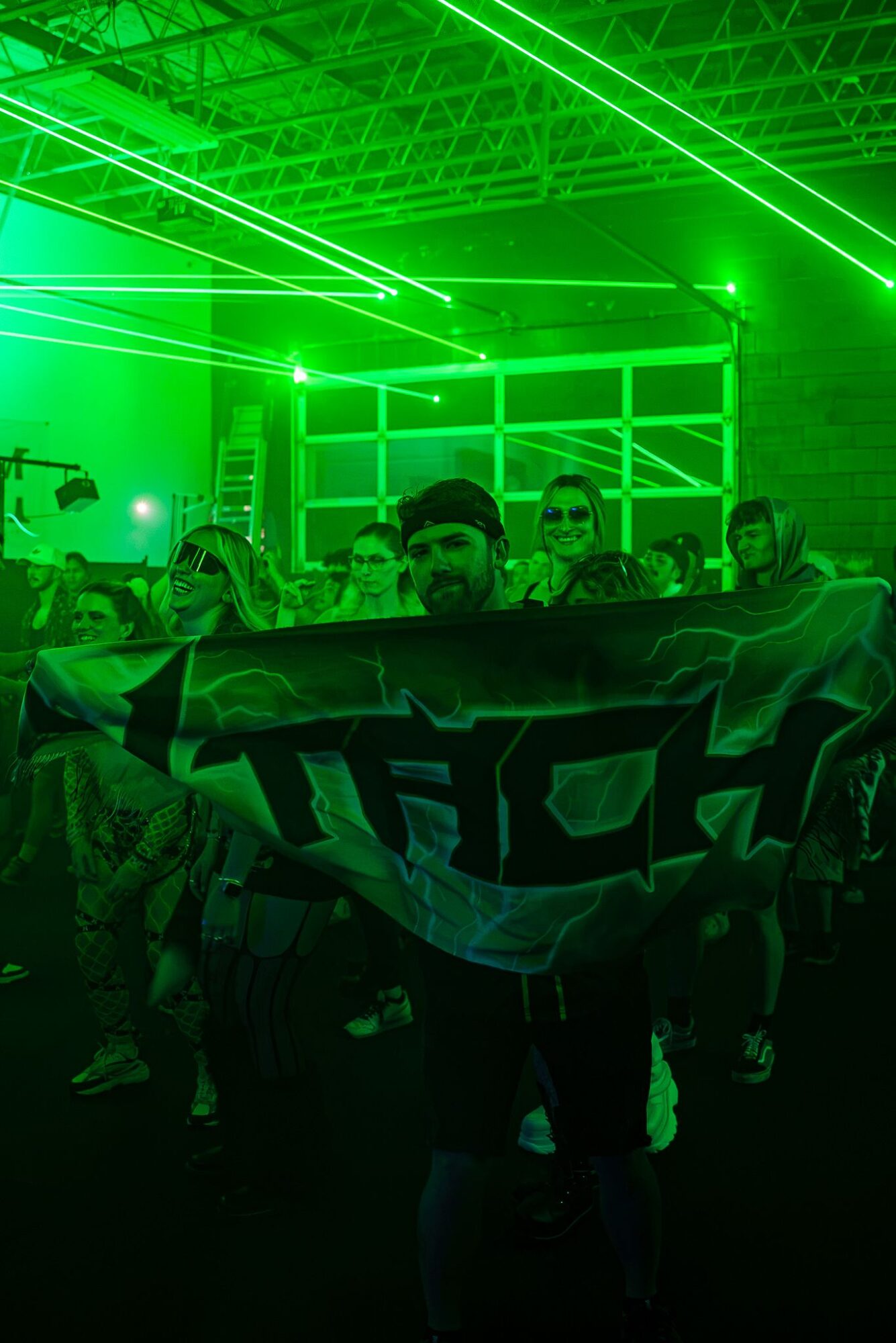 Group of people holding a banner in a venue with green laser lights and a grid-like background.