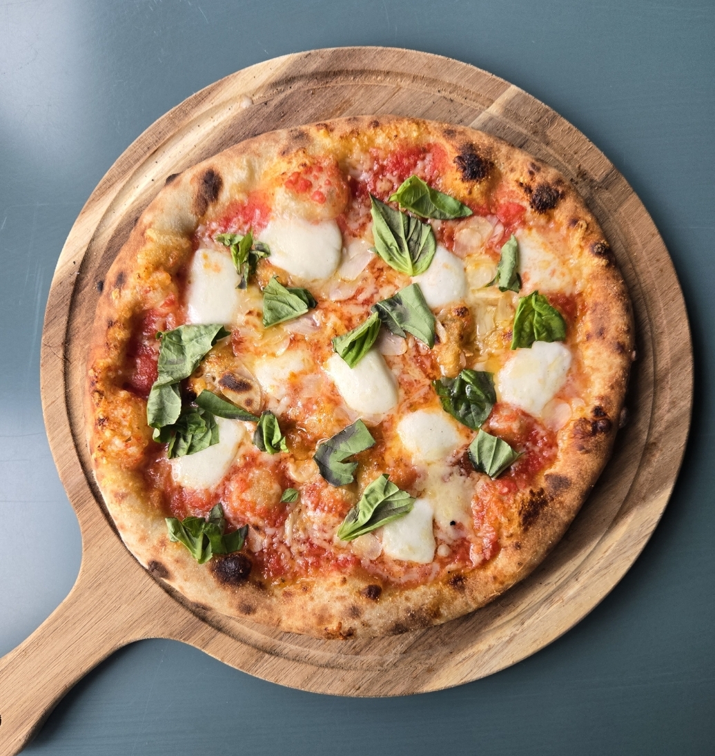 Pizza with cheese, basil, and tomato sauce on a wooden serving board, viewed from above.