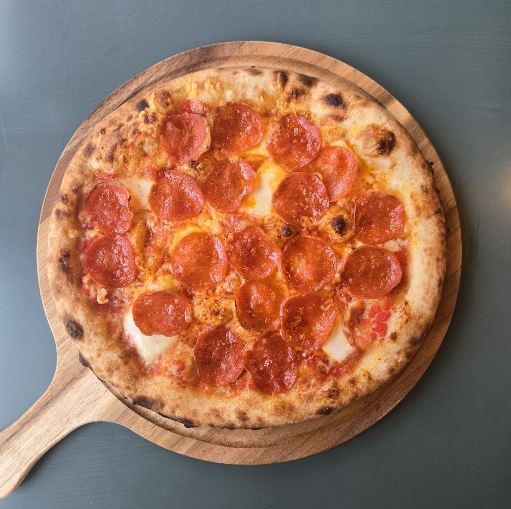 Pepperoni pizza on a wooden serving board with a blue background.
