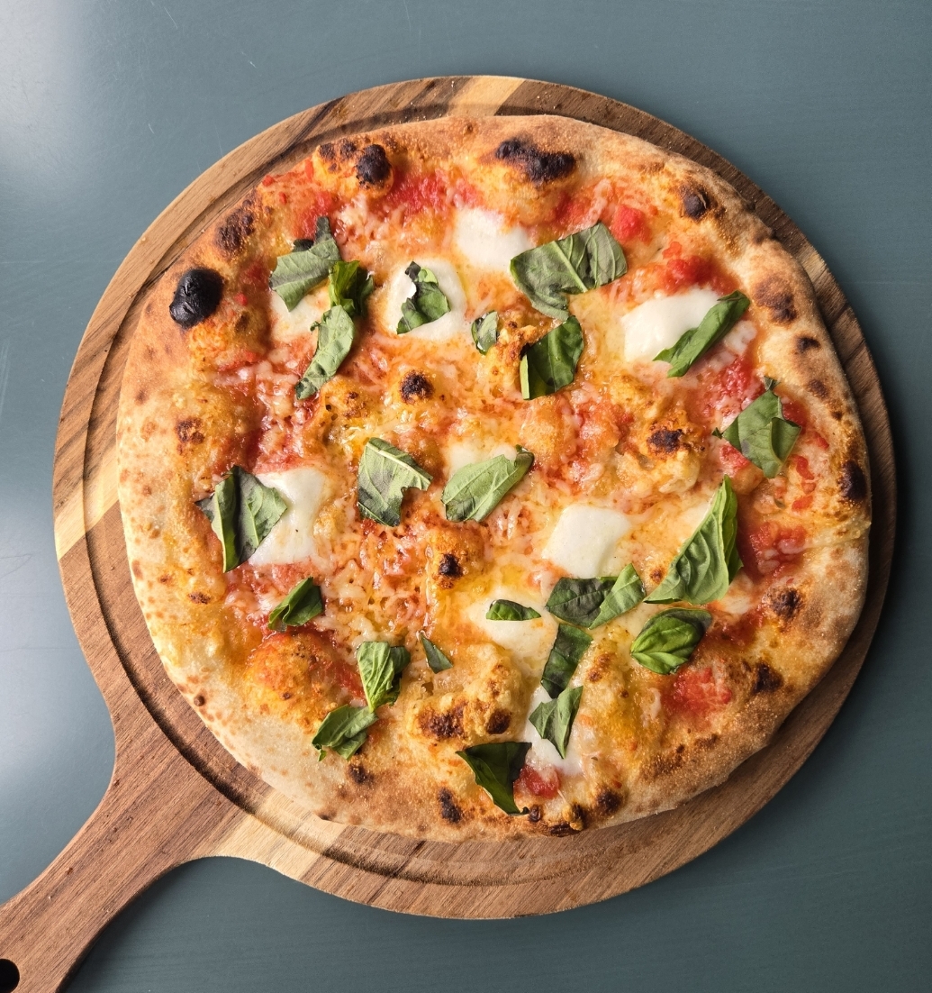 Pizza with cheese, tomato, and basil on a wooden serving board, viewed from above.