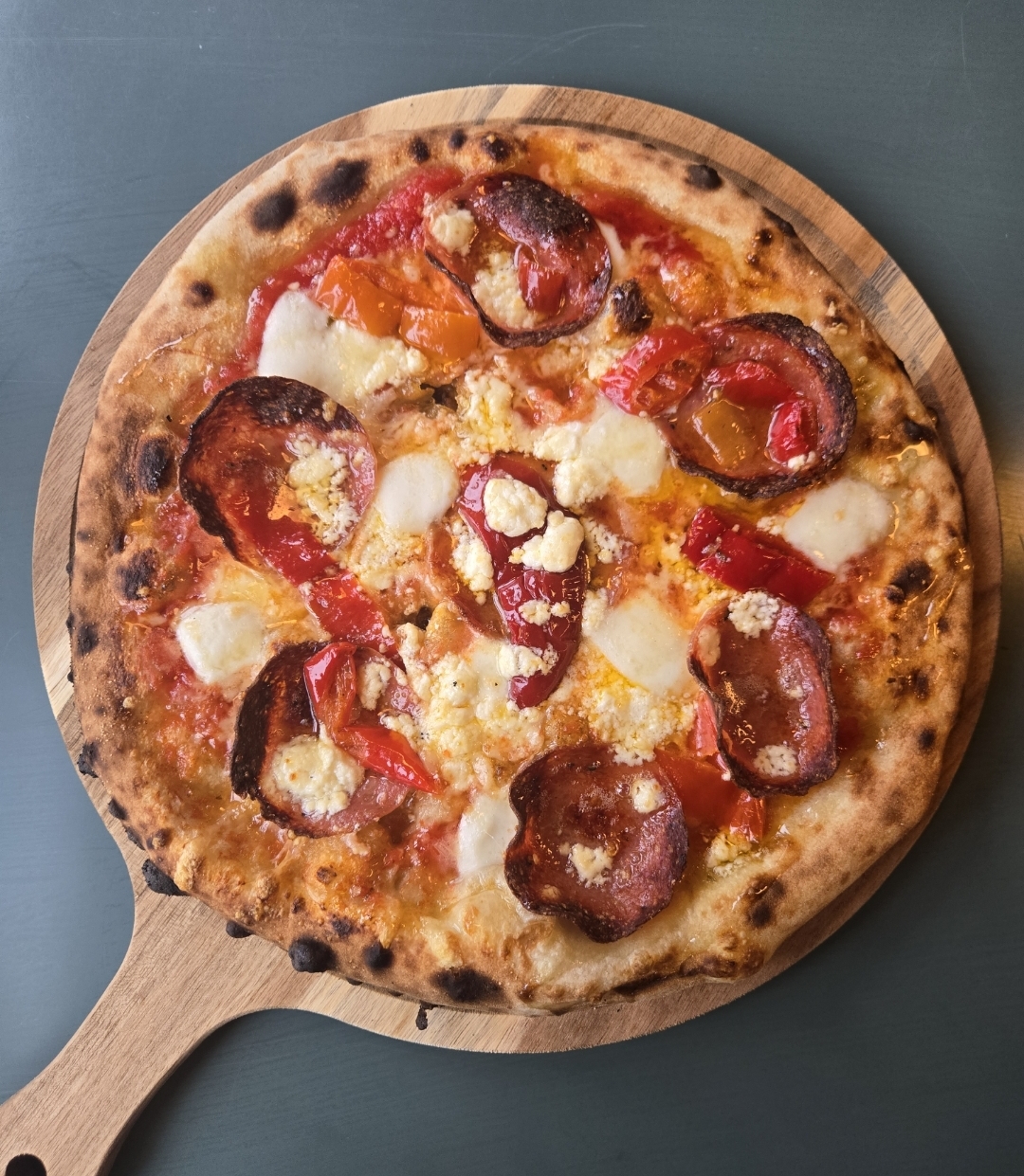 Pizza with pepperoni, red and yellow bell peppers, and cheese on a wooden serving board.