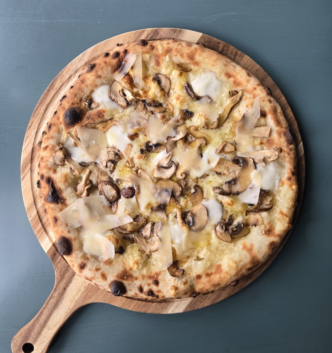 Pizza with cheese, mushrooms, and toppings on a wooden serving board, on a blue surface.