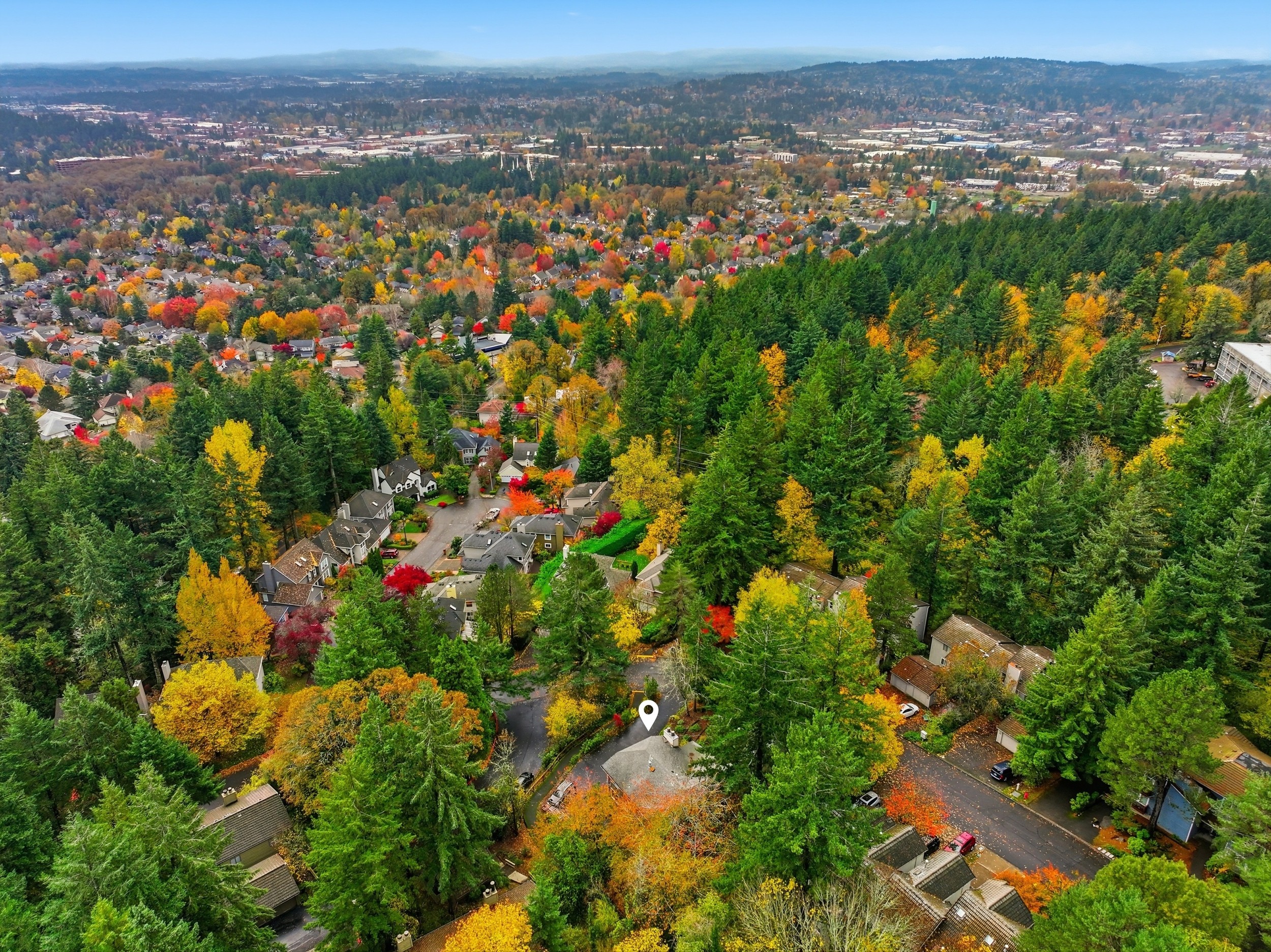 Aerial view of a neighborhood surrounded by colorful autumn trees, with houses and streets visible among the greenery.