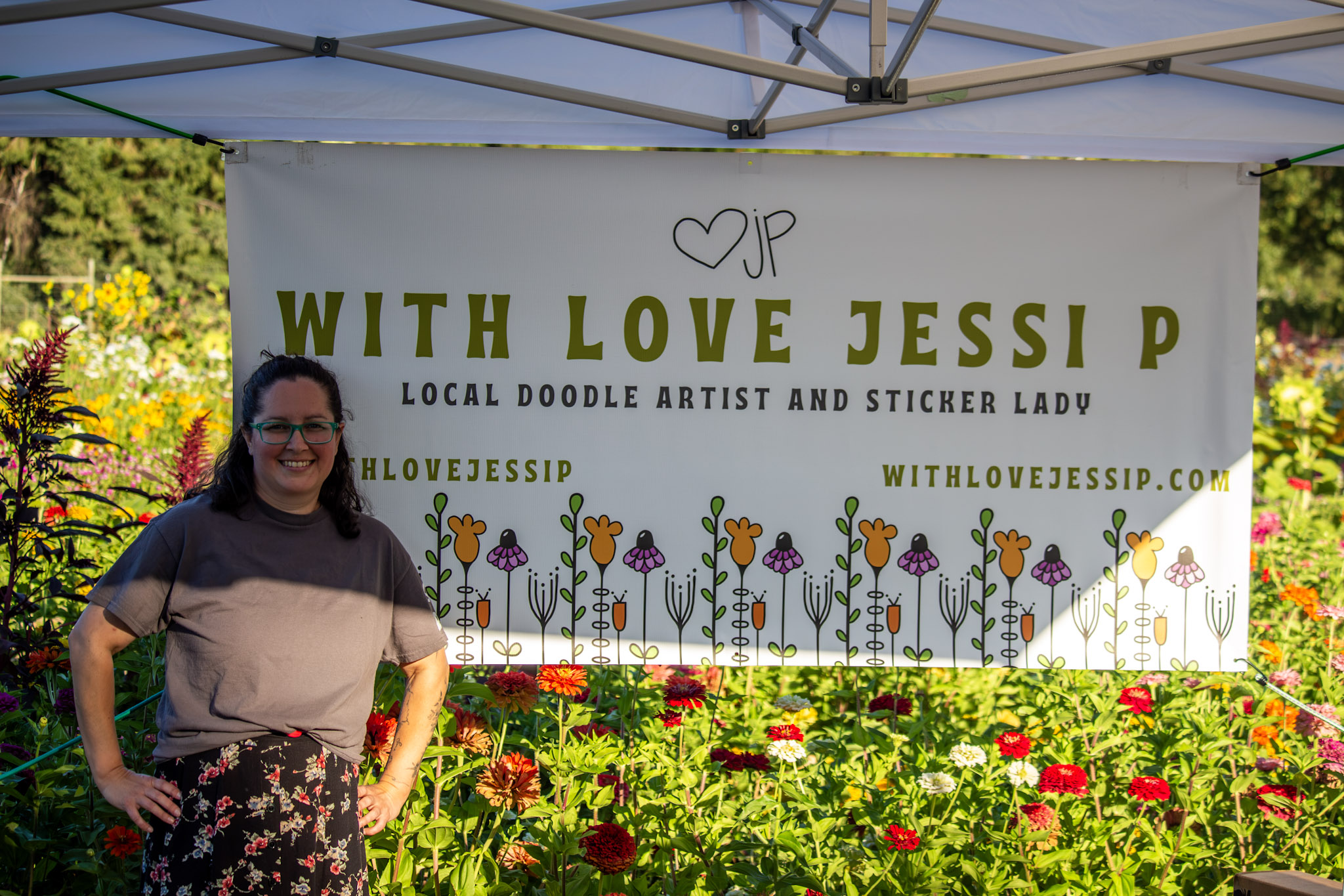 Woman standing in front of a garden with a large sign reading 'With Love Jessi P' and decorative flowers.