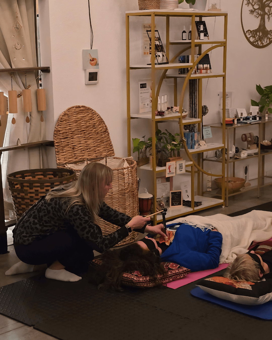 Woman providing first aid to a person lying on the floor indoors, with shelves and plants in the background.