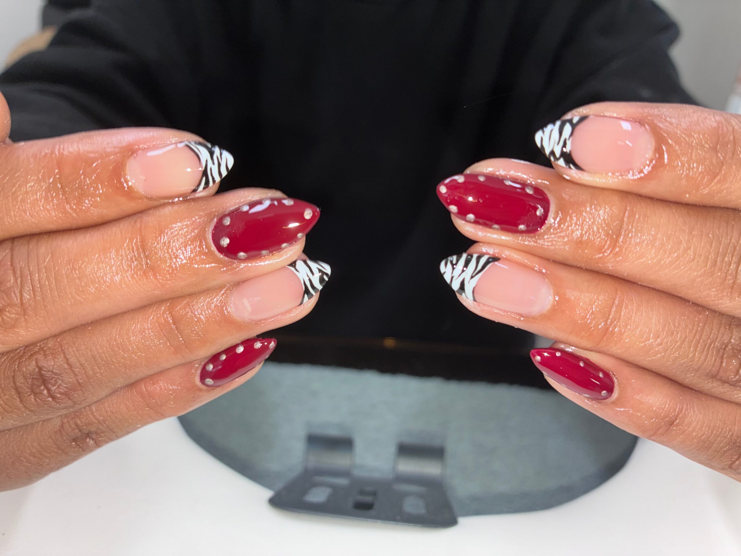 Person's hands with decorated nails, red and zebra pattern, holding a black object, background blurred.