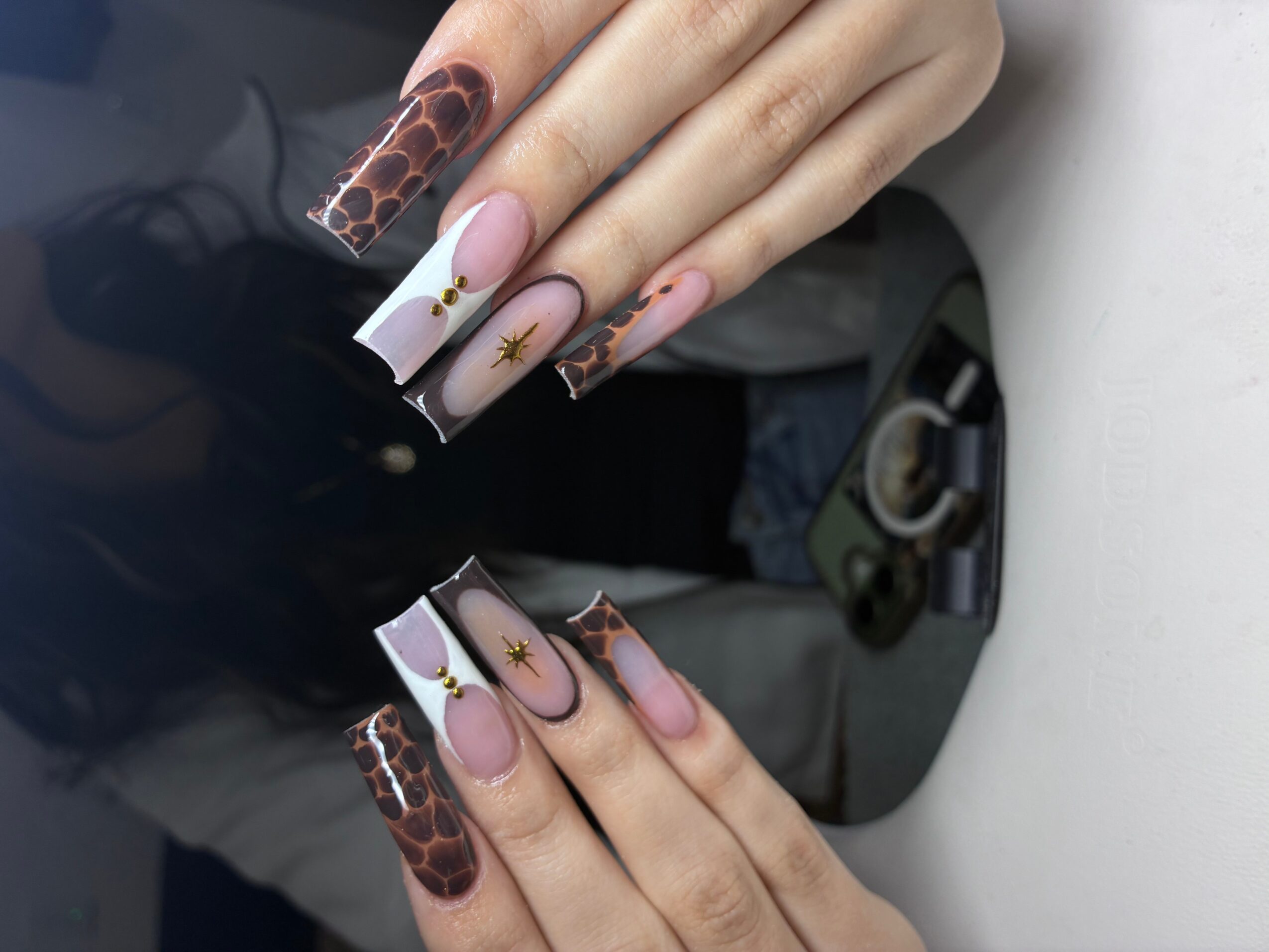 Close-up of hands with long, decorated nails featuring animal print, gold accents, and pink designs, resting on a white surface.