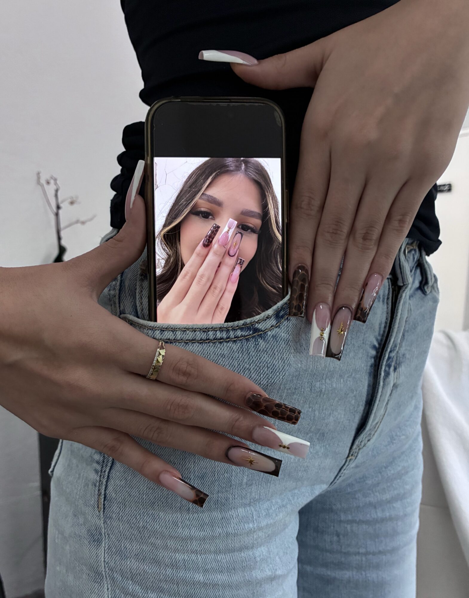 Person holding a phone with a woman's face on the screen, covering her mouth with her hand, in front of their jeans.