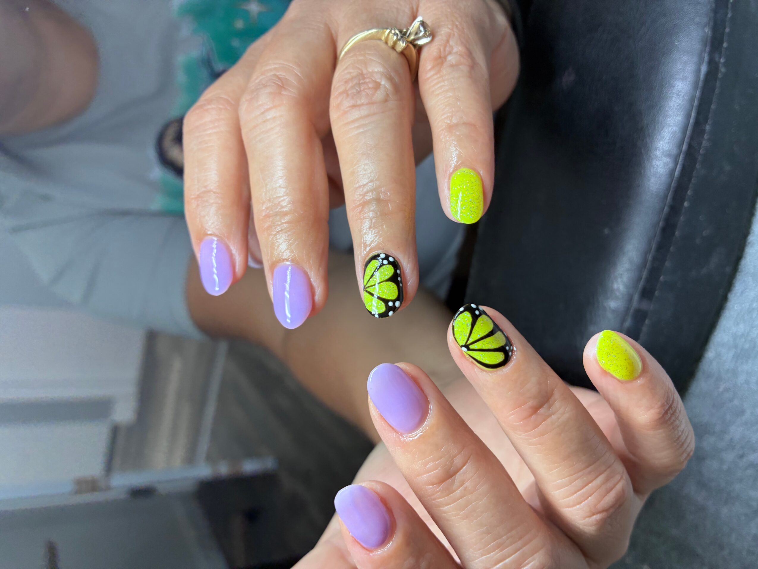 Hands with colorful nail polish and butterfly nail art, one hand with purple nails and the other with yellow nails.