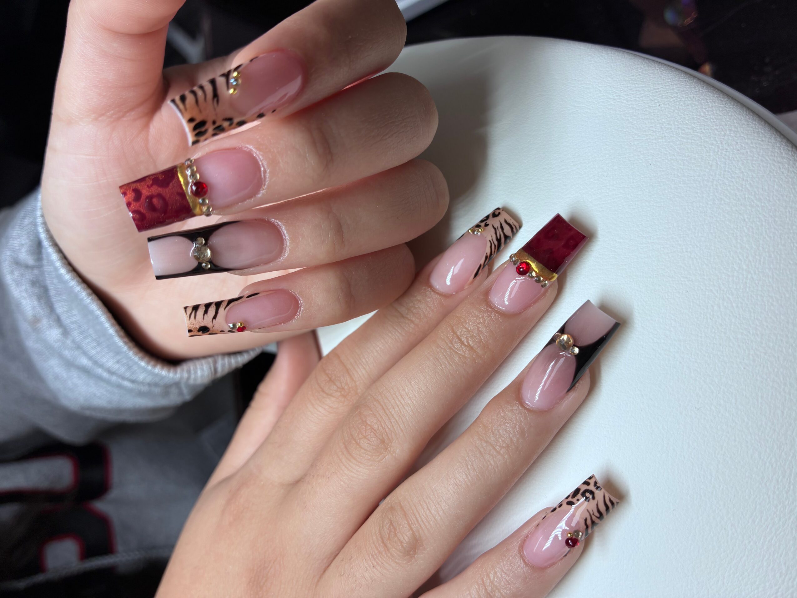 Close-up of hands with decorated nails, some with red and leopard print designs, resting on a white surface.