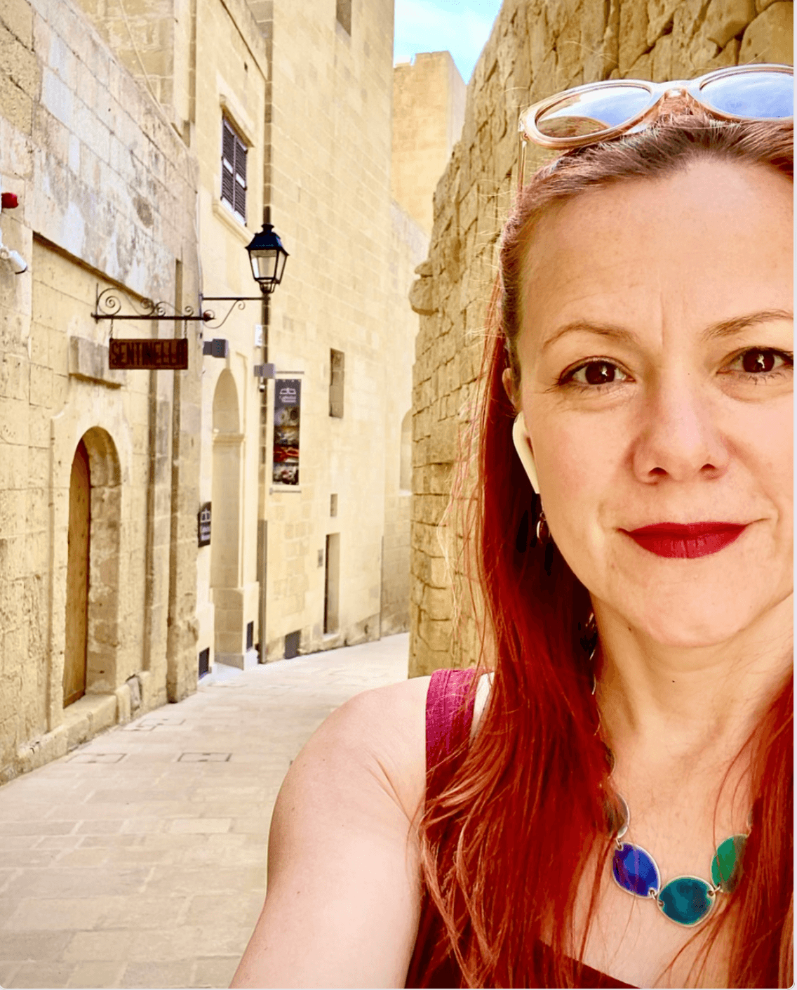 Person with red hair taking a selfie in a narrow stone-paved alley lined with historic buildings.