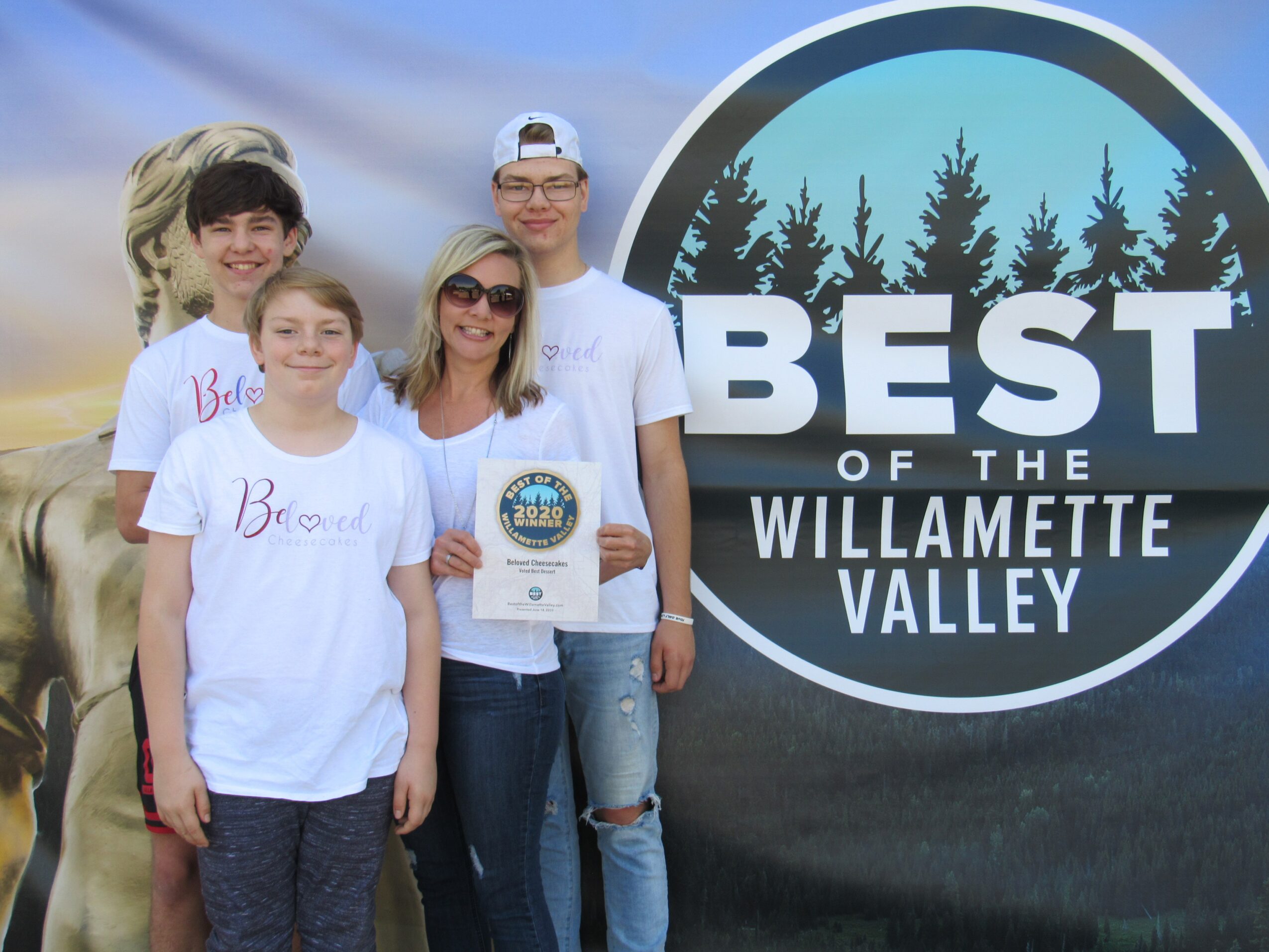 Four people standing outdoors in front of a large circular sign that reads 