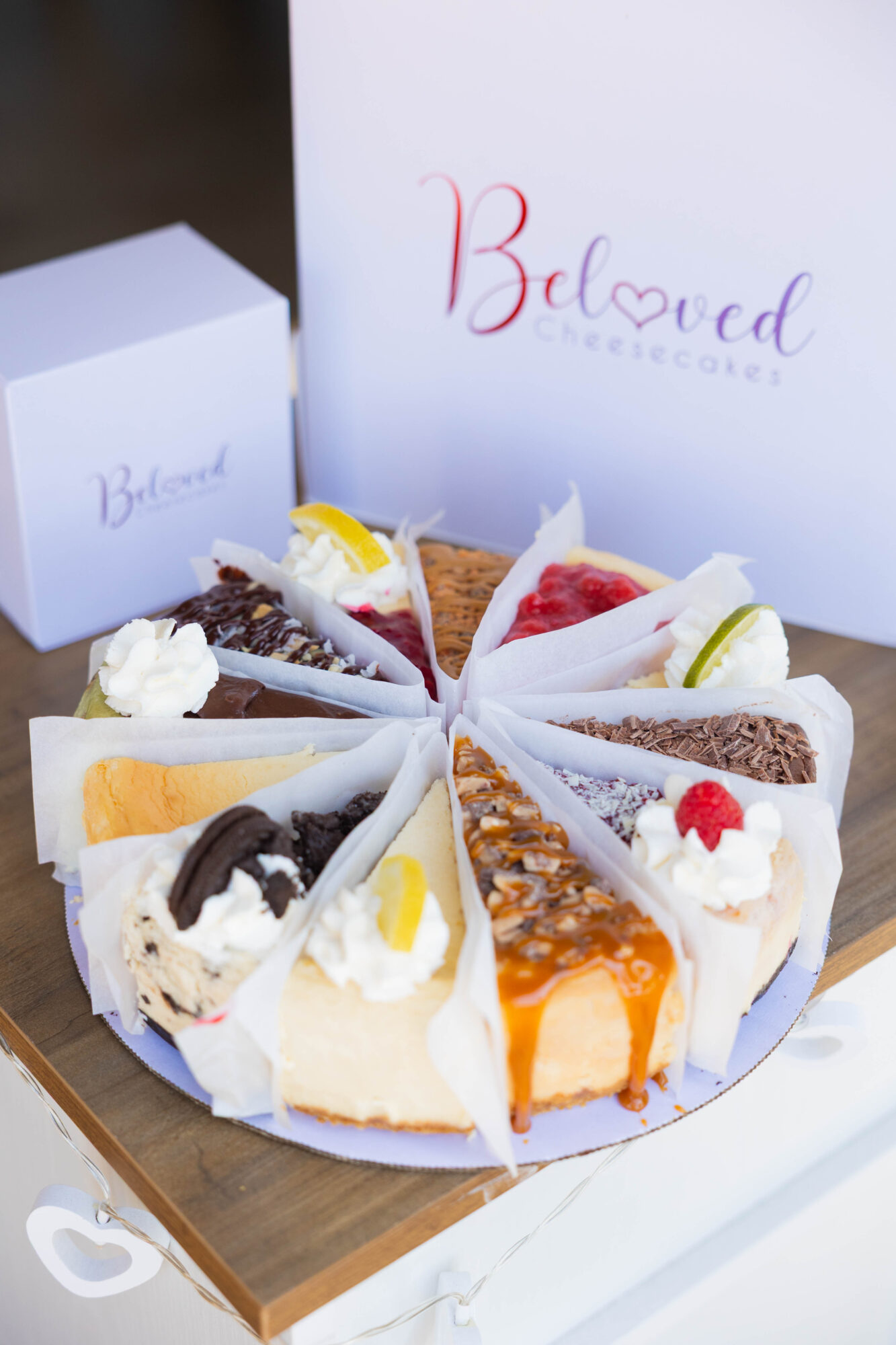 Assorted slices of cake arranged on a white plate, with a white box and a sign in the background.