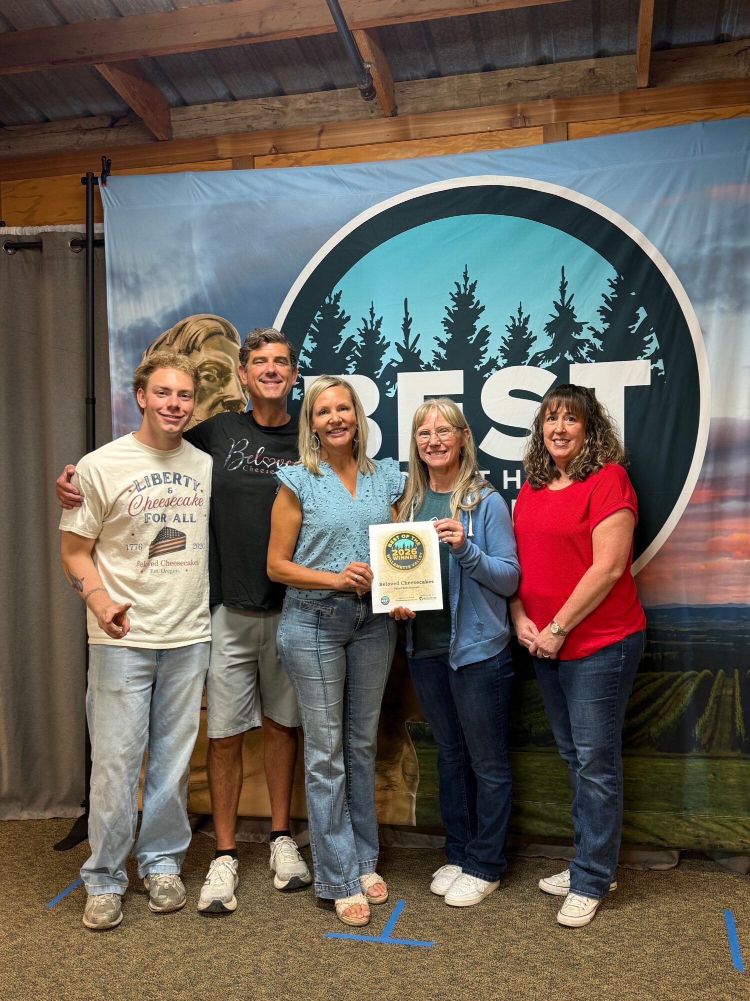 Four people standing in front of a circular logo with trees and the word 'YES'. One person holds a certificate.