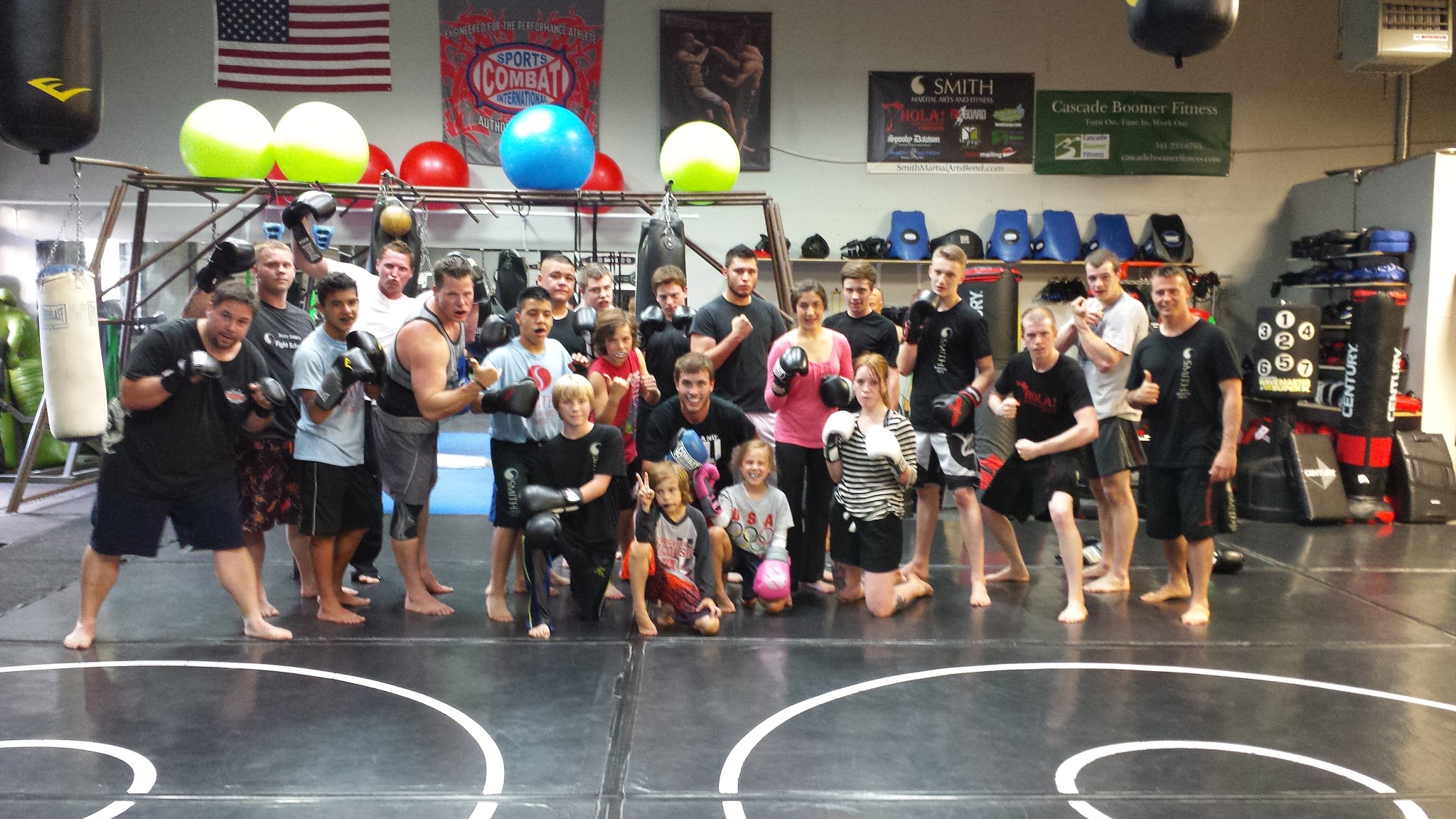 Group of people, including children and adults, in a gym with boxing equipment and colorful balls, posing for a photo.