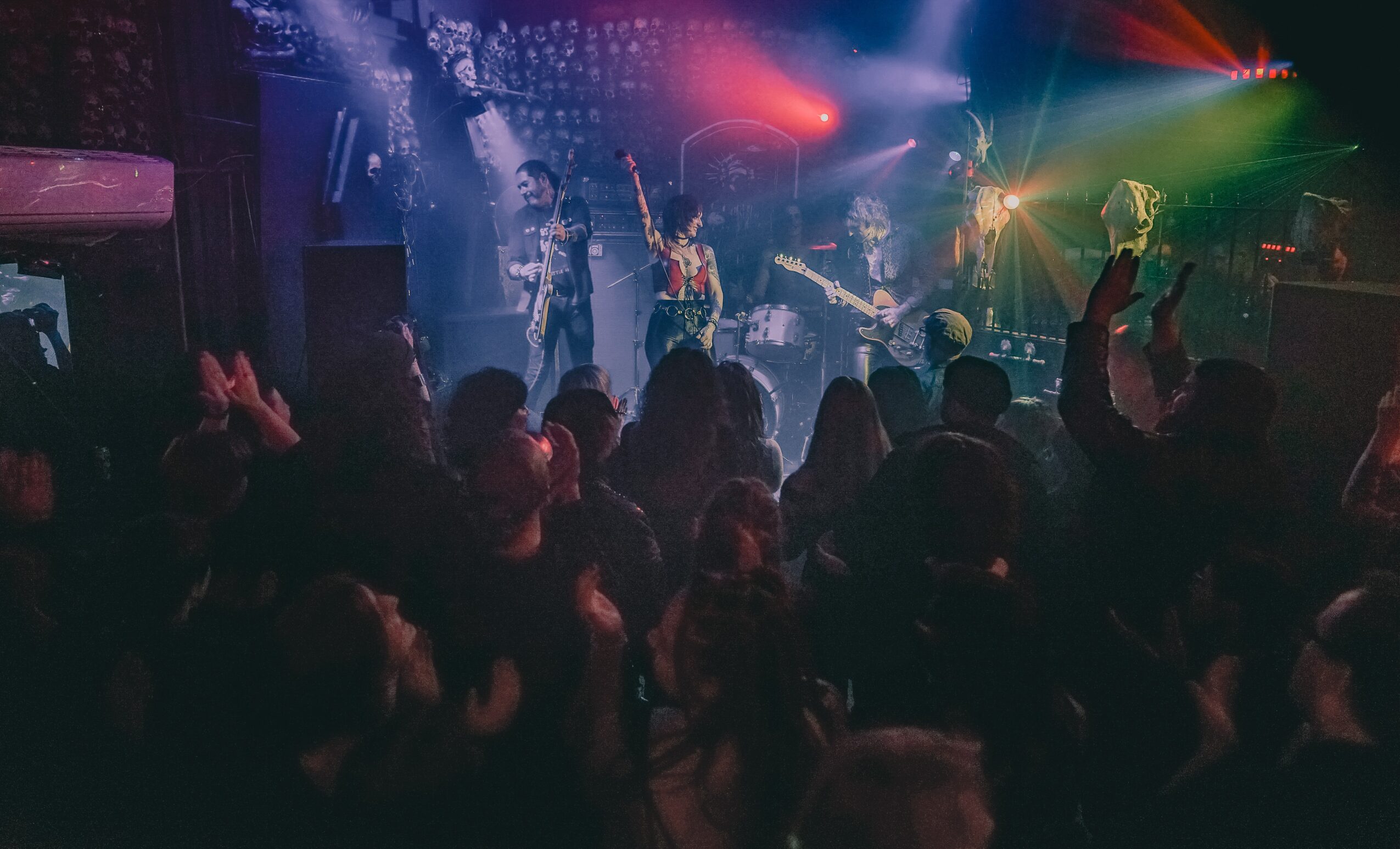 A crowd watches a band performing on a stage under colorful lights.