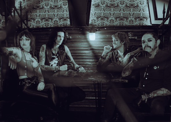 Four people sit around a table in a dimly lit room with patterned wallpaper.