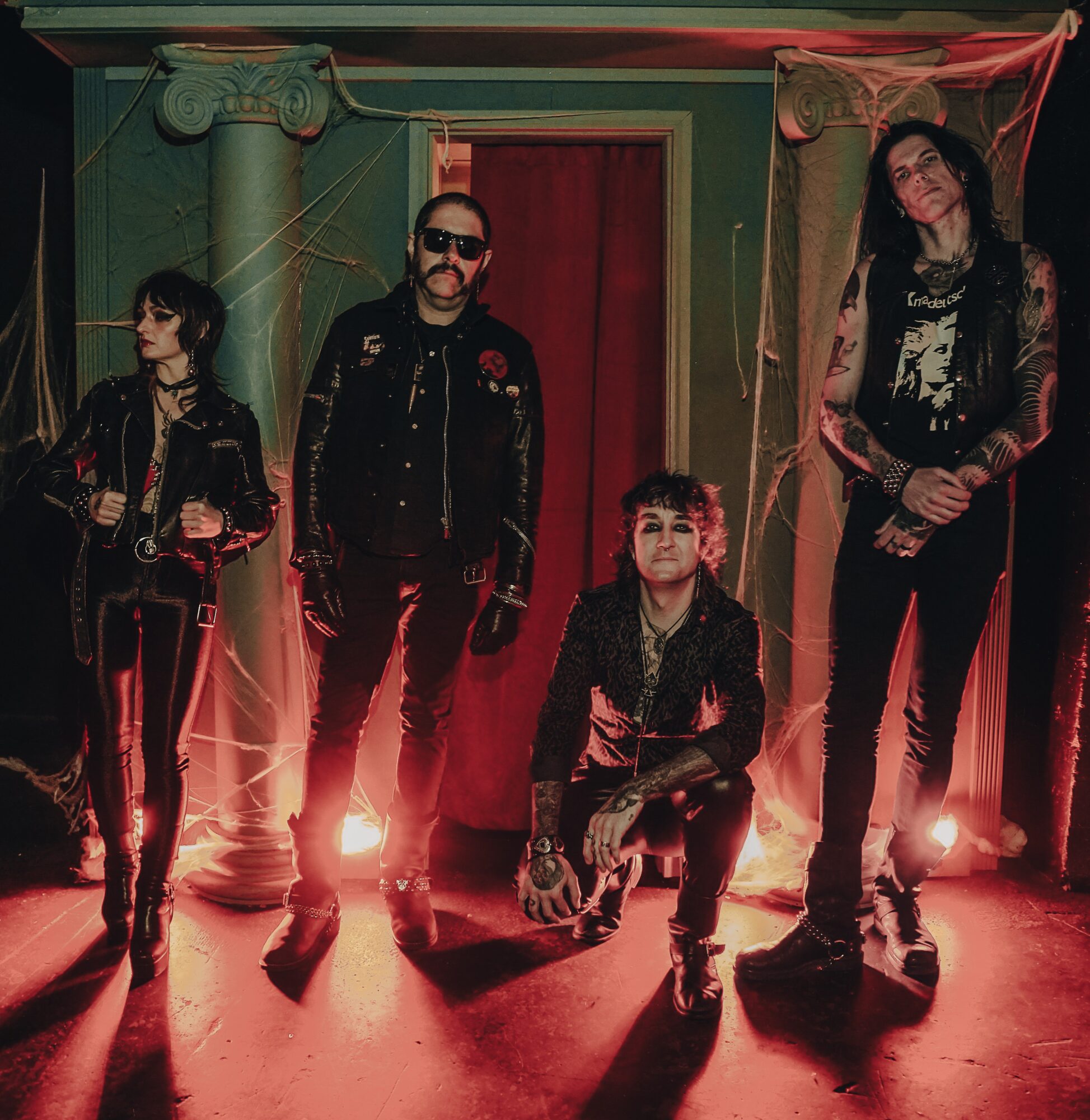 Four people pose in a dim room with red lighting, columns, and a doorway.