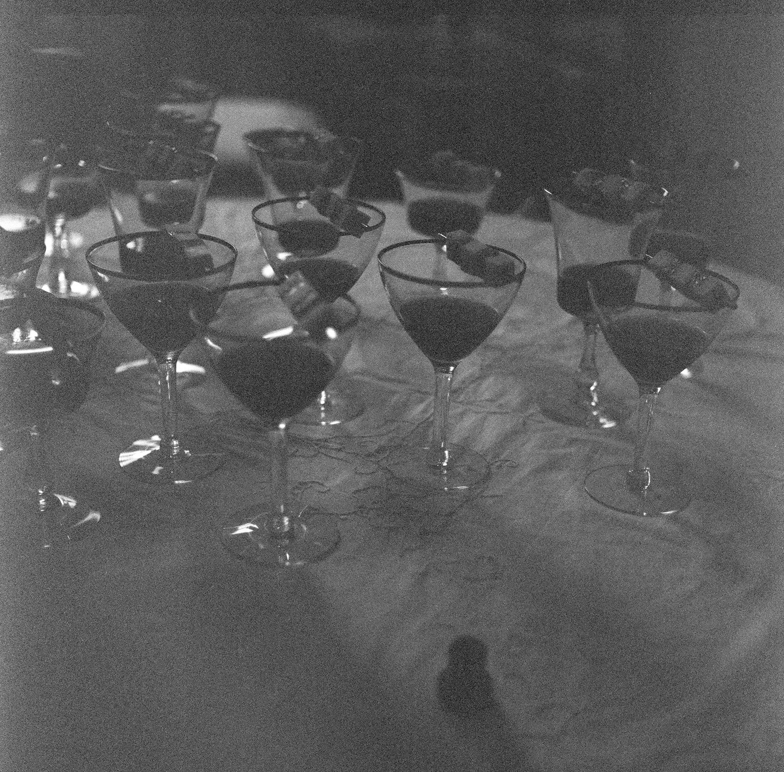 Multiple cocktail glasses filled with dark liquid arranged on a table, some glasses overlapping, in black and white.