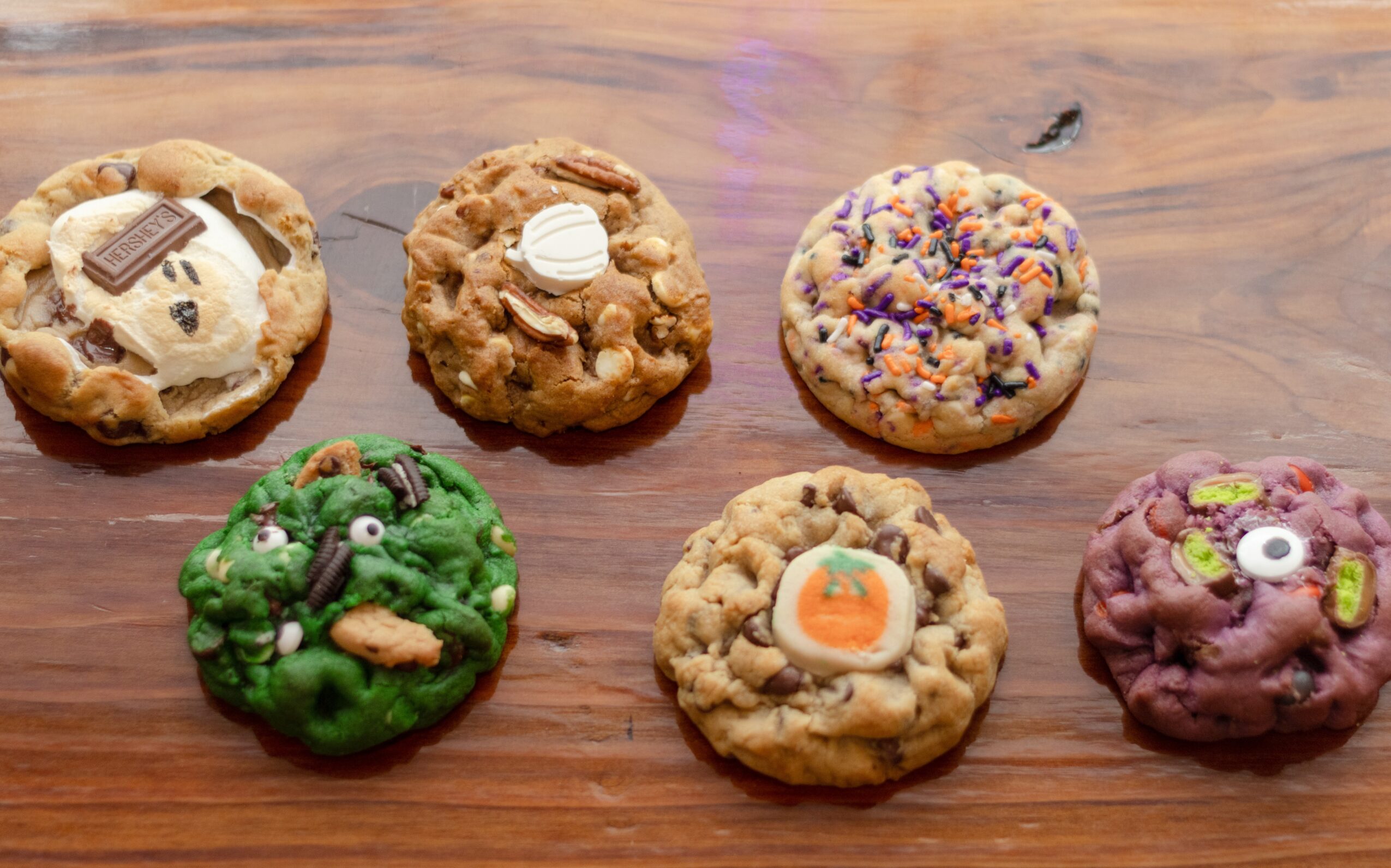 Six decorated cookies on a wooden surface, each with different toppings and colors.