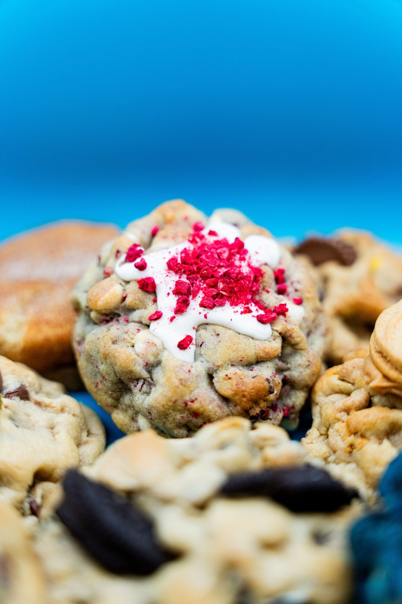 Close-up of assorted cookies with colorful toppings and fillings, set against a blue background.