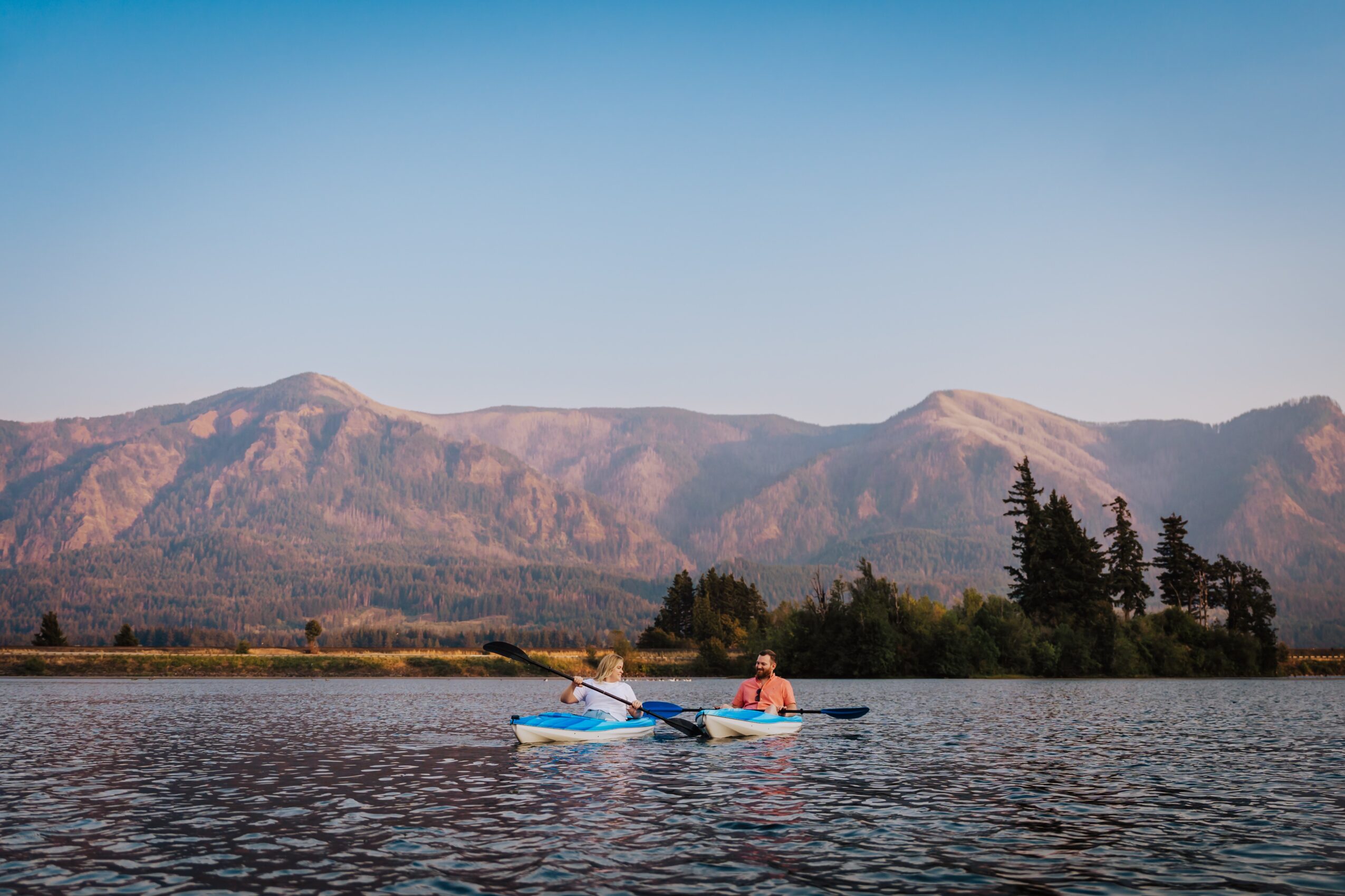 Person kayaking on a lake with mountains in the background under a clear sky.