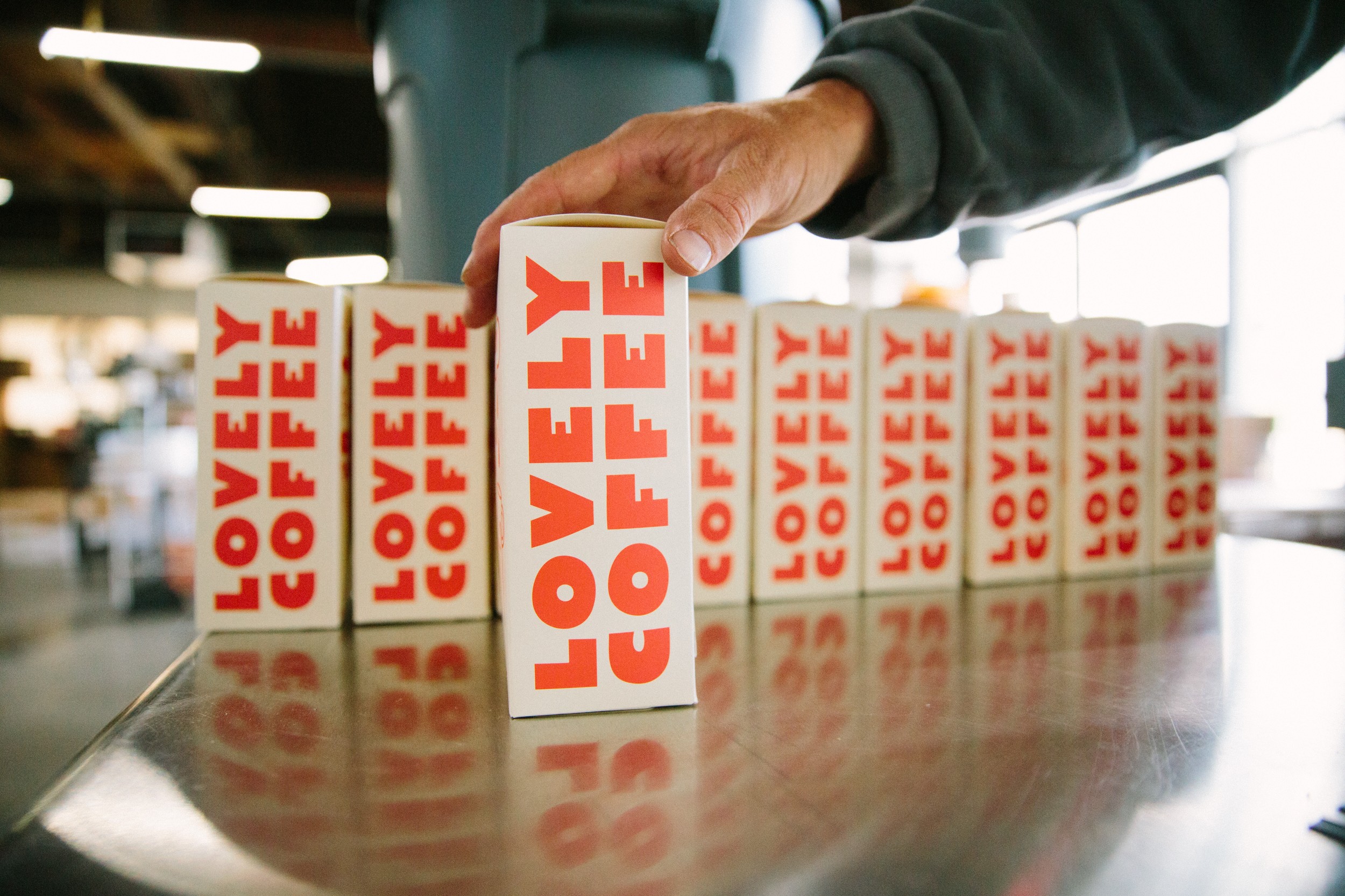 Person's hand reaching for a row of white boxes with red text reading 'LOVE COFFEE' on a reflective surface.