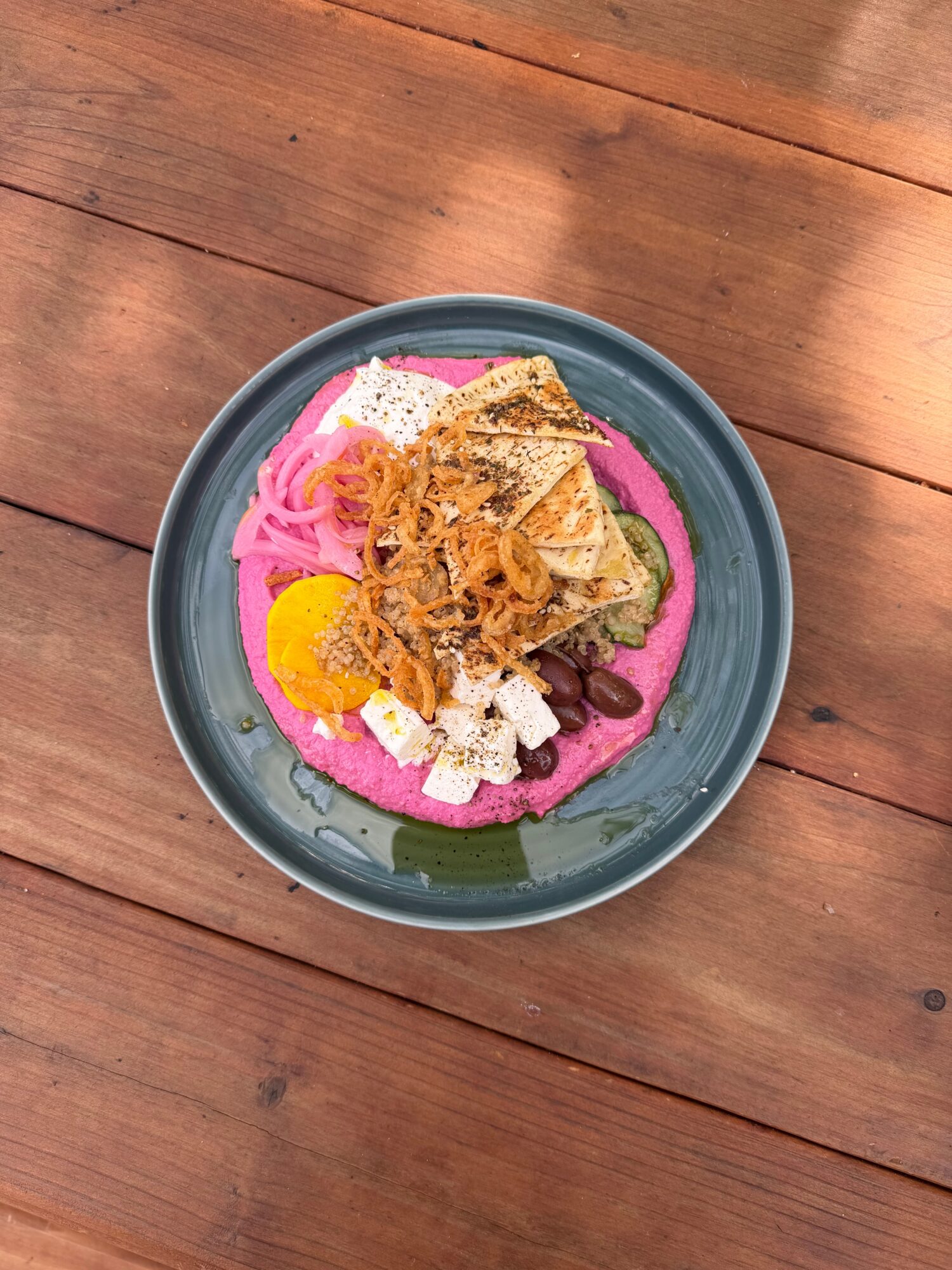 Bowl with pink smoothie topped with granola, banana slices, and other toppings on wooden surface.