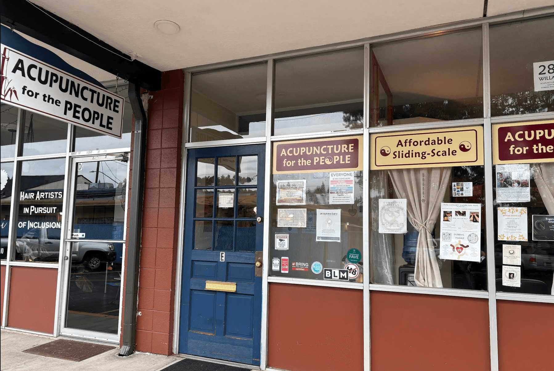 Storefront with blue entrance door, windows, and acupuncture and affordable sliding-scale service signs.