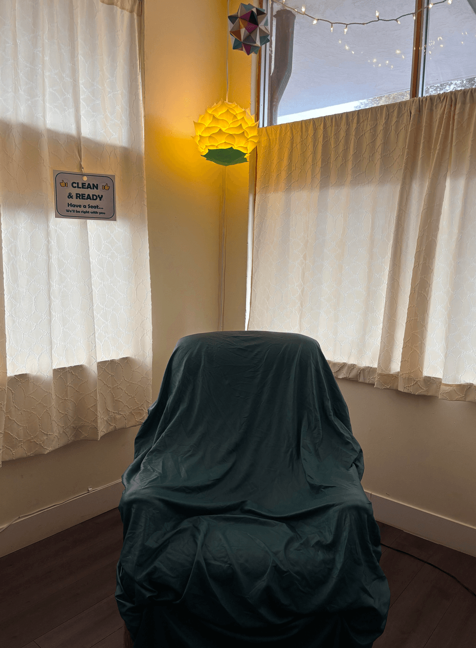 A dark cloth drapes over a chair between curtained windows, with a yellow hanging lamp above.
