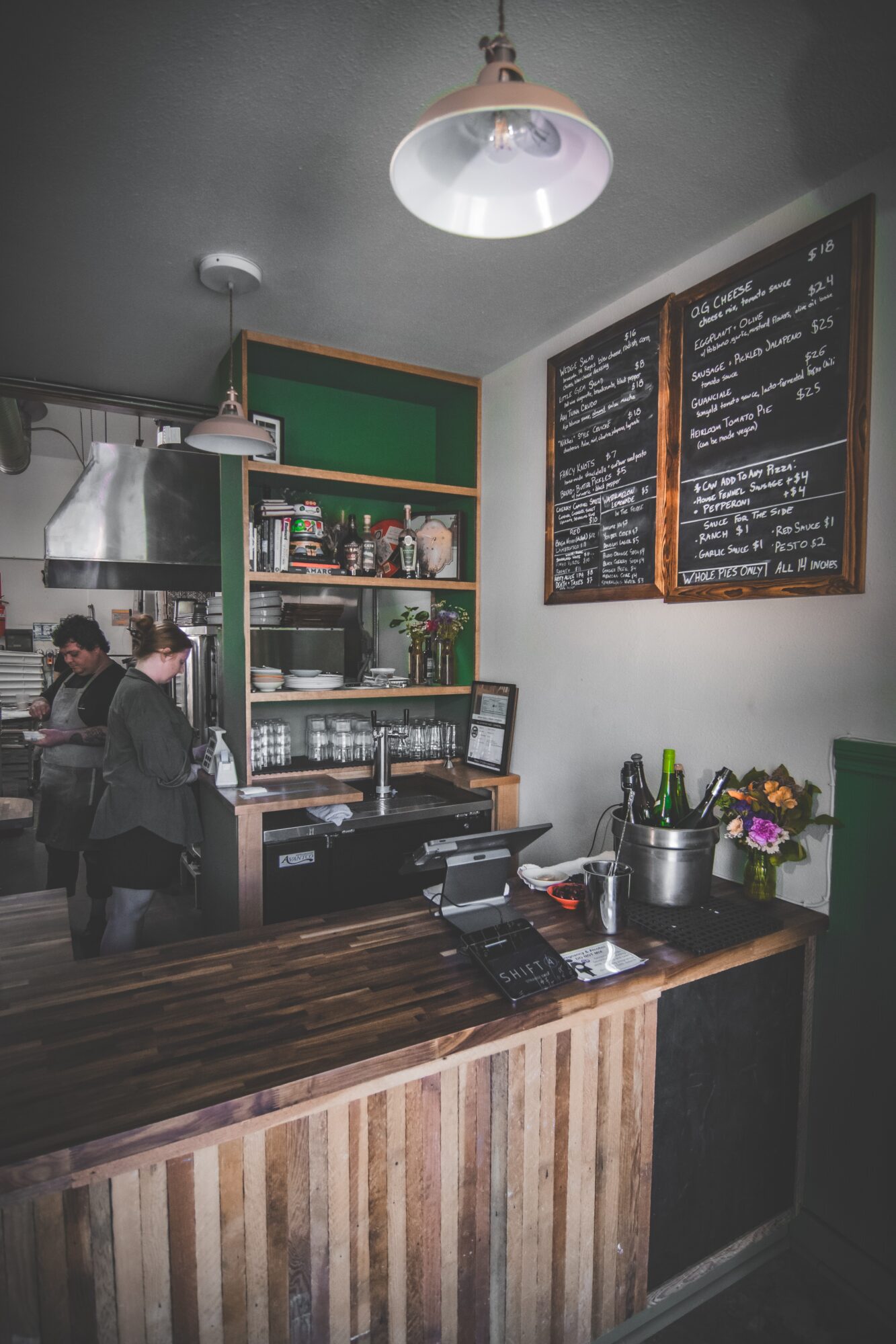 Interior of a cafe with a wooden counter, shelves with bottles, and a chalkboard menu on the wall.
