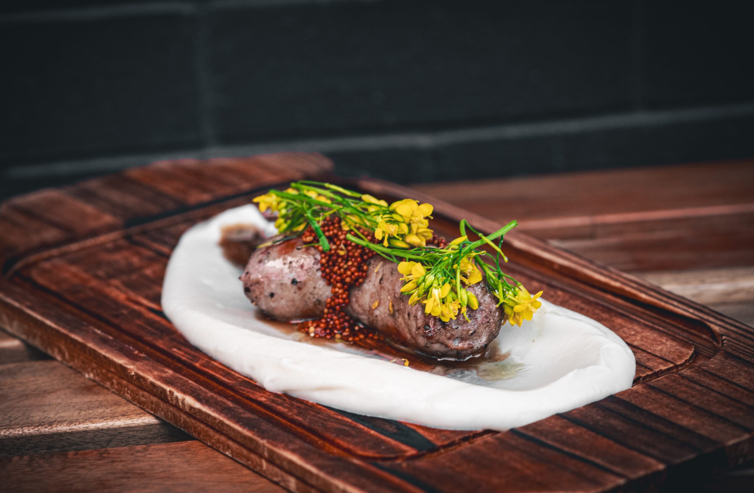 A plated dish with a rolled meat, garnished with yellow flowers and herbs, on a wooden serving board.