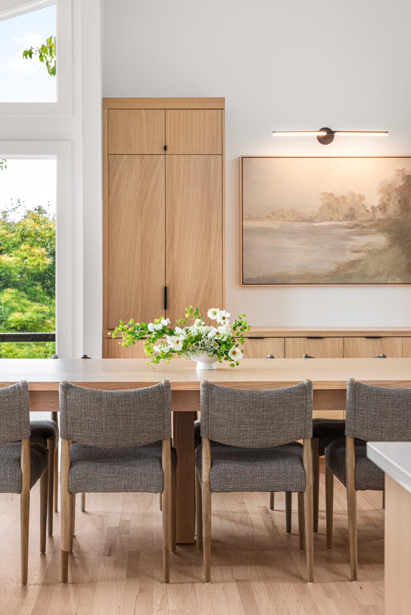 Dining room with wooden table, six chairs, a cabinet, and a landscape painting on the wall.