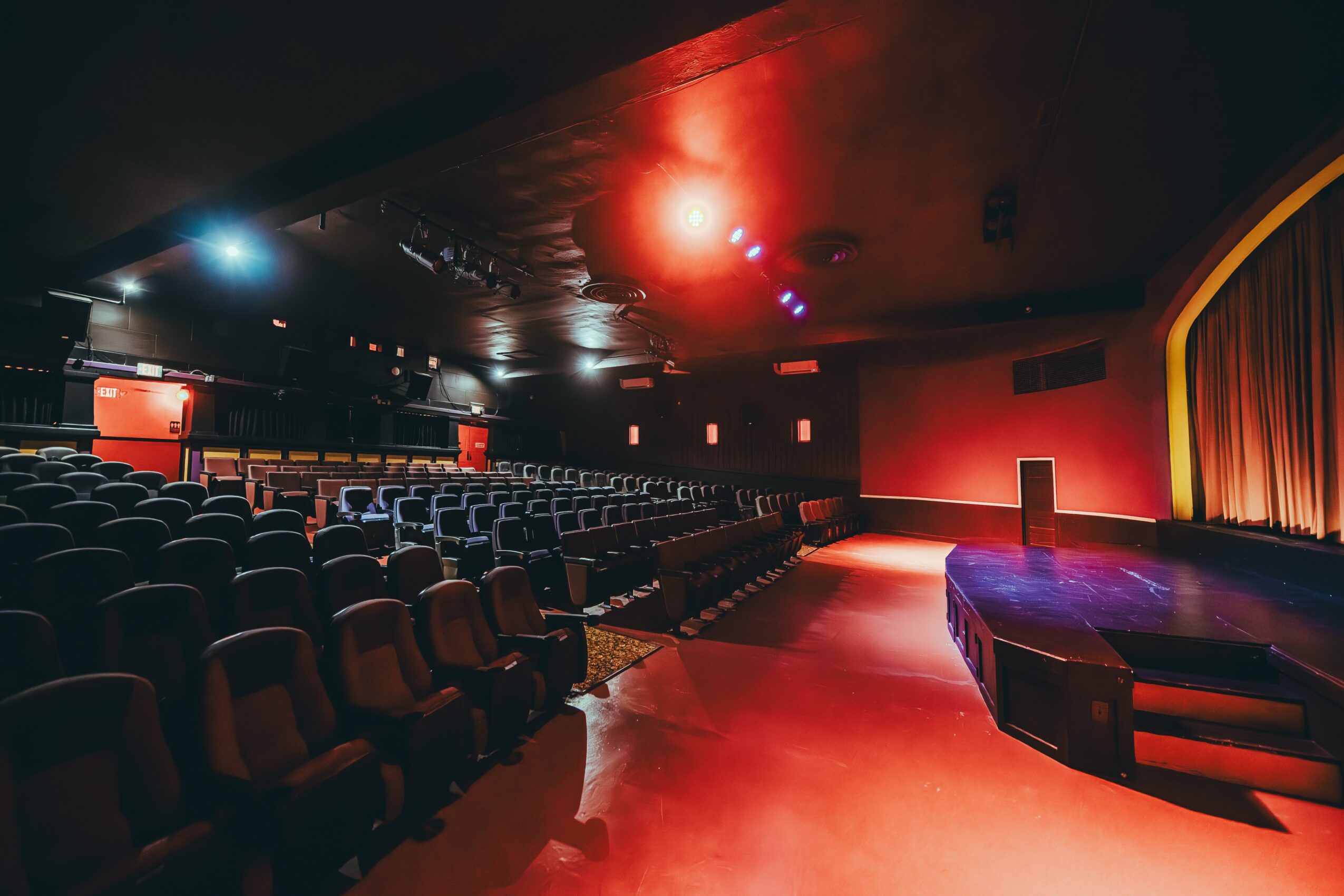 Empty theater with rows of seats, stage with curtain, and dim lighting, ready for a performance.