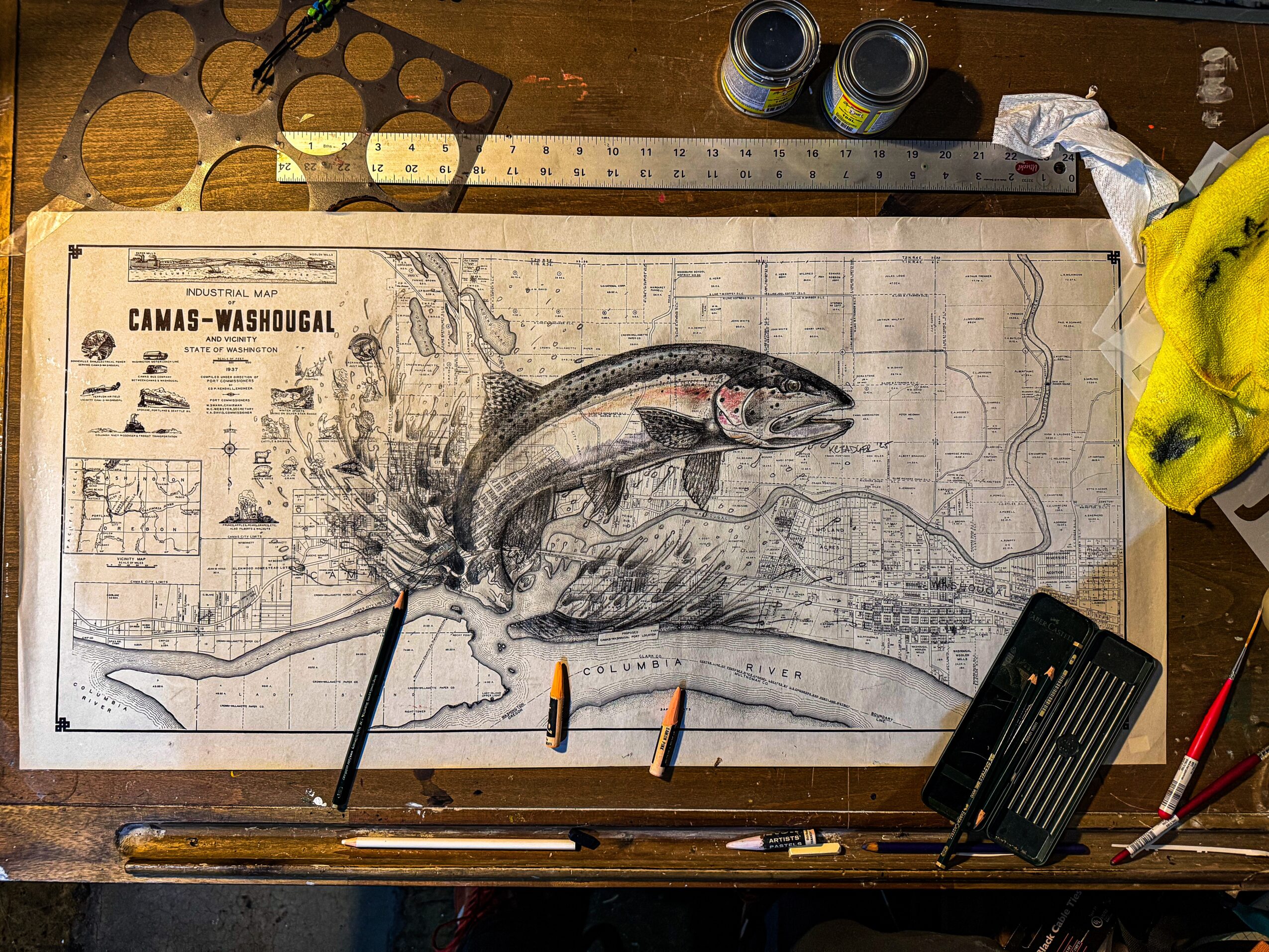 Detailed map with a large fish illustration, tools, and supplies on a wooden table, including pens, a ruler, and cans.