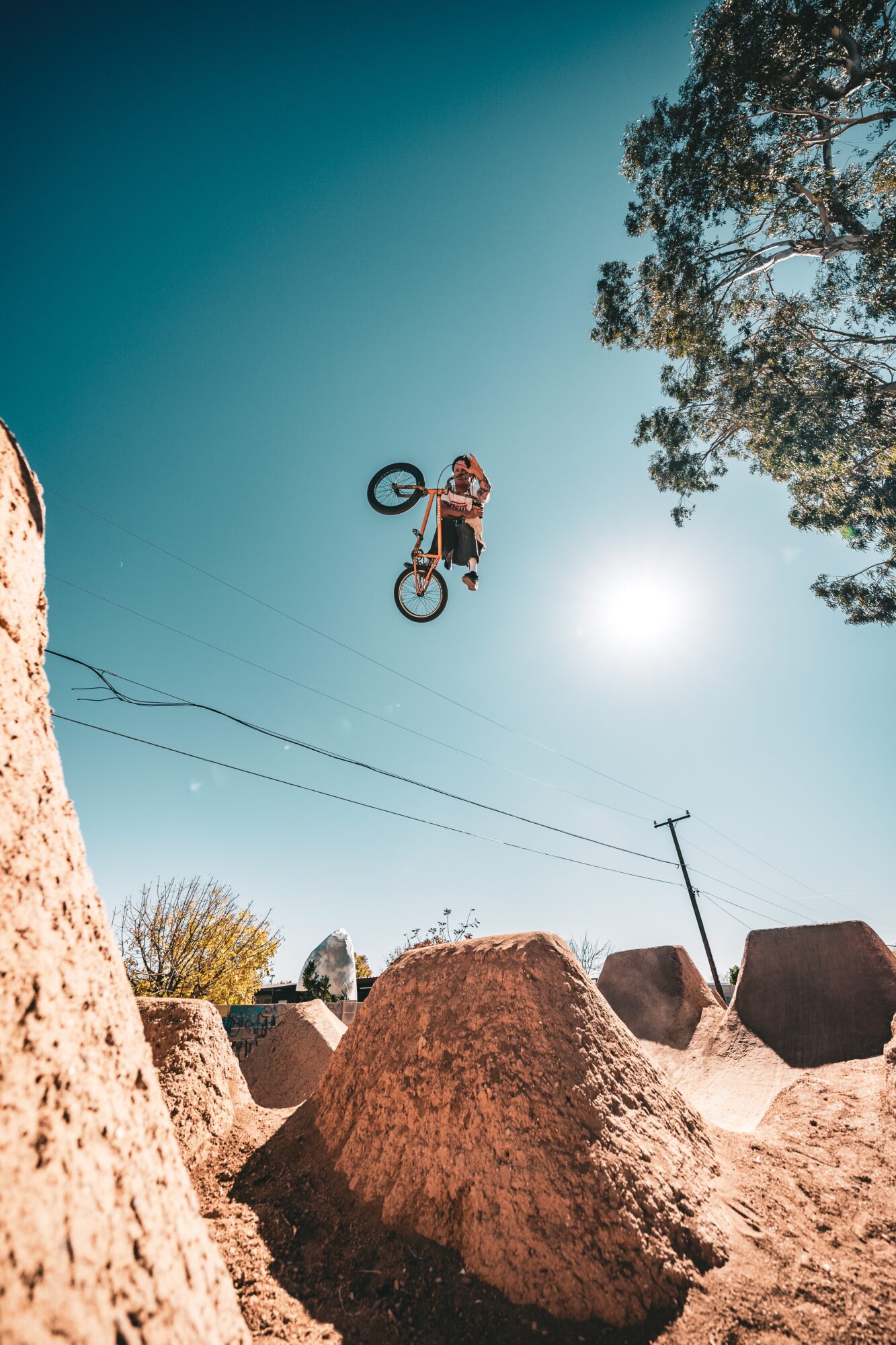 Person performing a mid-air stunt on a bicycle against a clear sky with trees and rocks below.