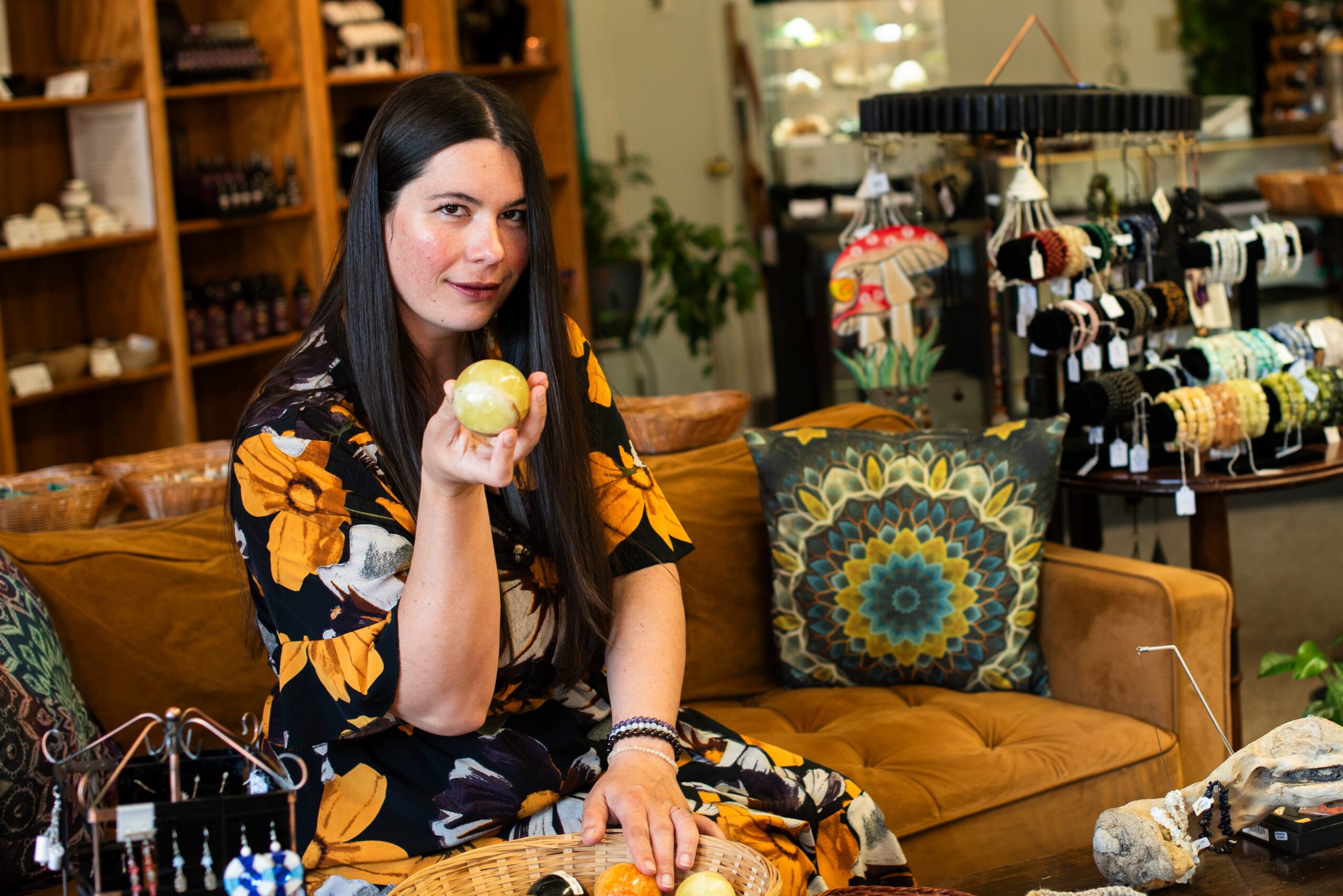 Woman with long dark hair holding a yellow apple in a store with shelves of yarn and a sofa with a decorative pillow