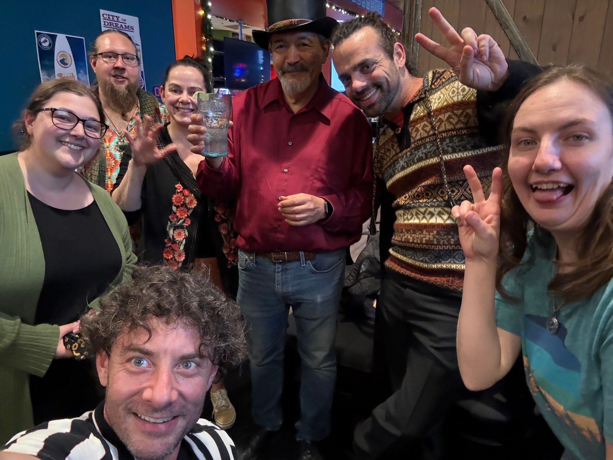 Group of people smiling and making peace signs, gathered indoors with a woman in a red top in the center.