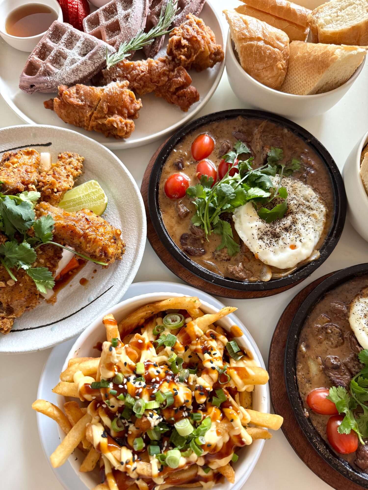 Assorted dishes including fried chicken, bread, pasta with sauce, and a bowl of soup with cherry tomatoes and greens.