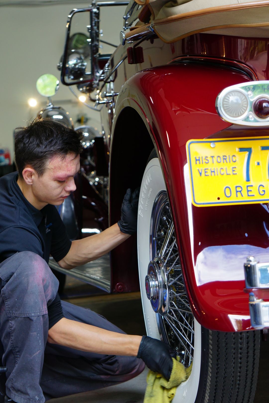 A person crouches beside a red motorcycle with a yellow historic vehicle license plate.