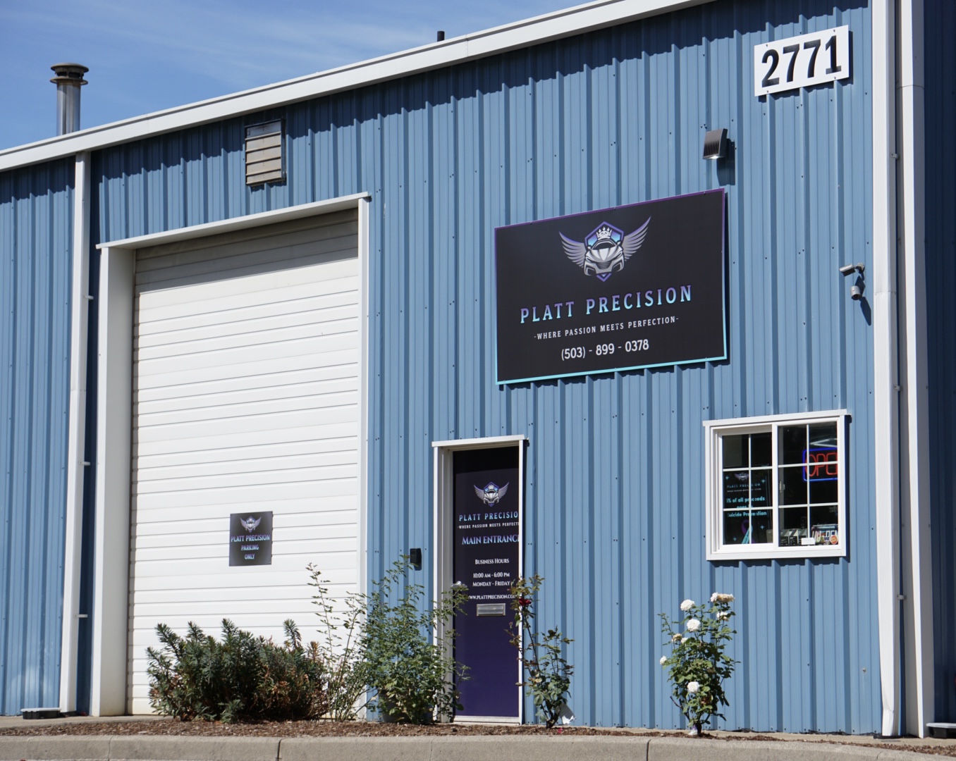 Blue metal-sided commercial building with a roll-up door, windows, and a sign reading “Platt Precision.”