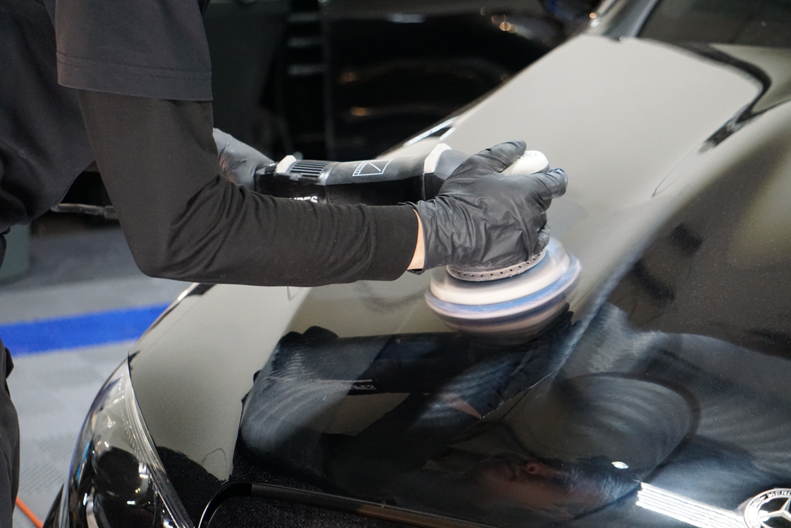 A person uses a handheld polisher on the hood of a car.