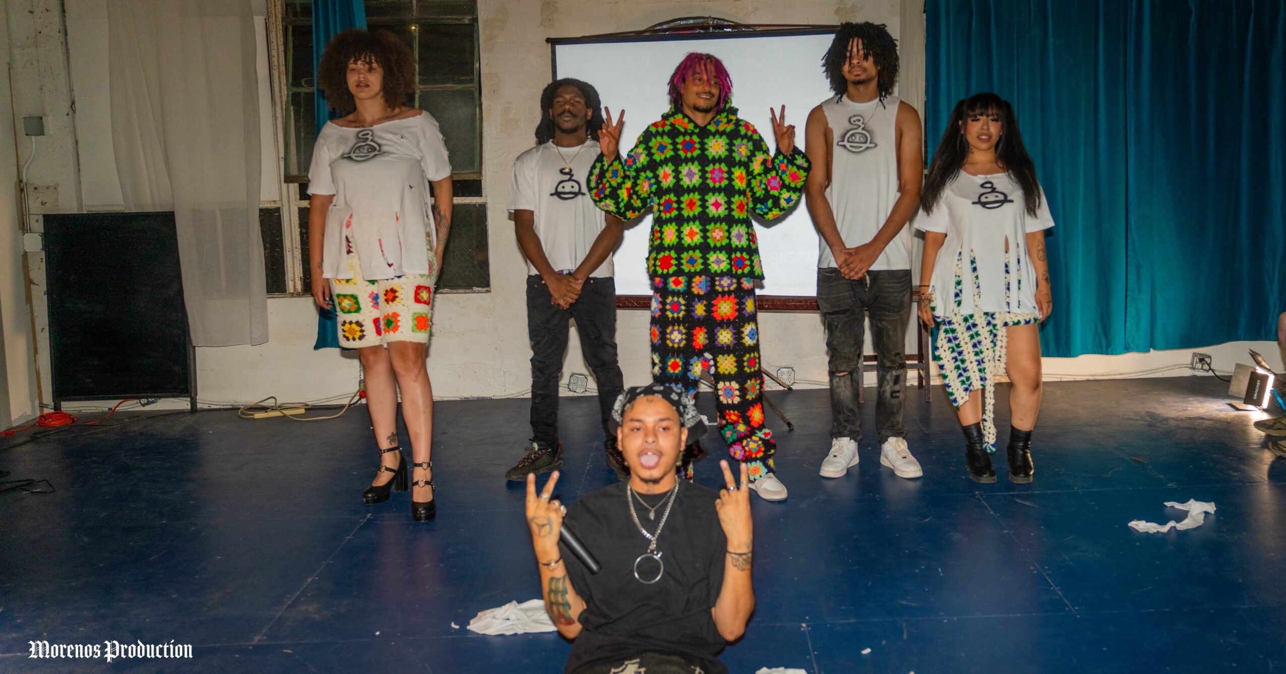 A group of six people pose in a room, with one person seated in front and five standing behind.