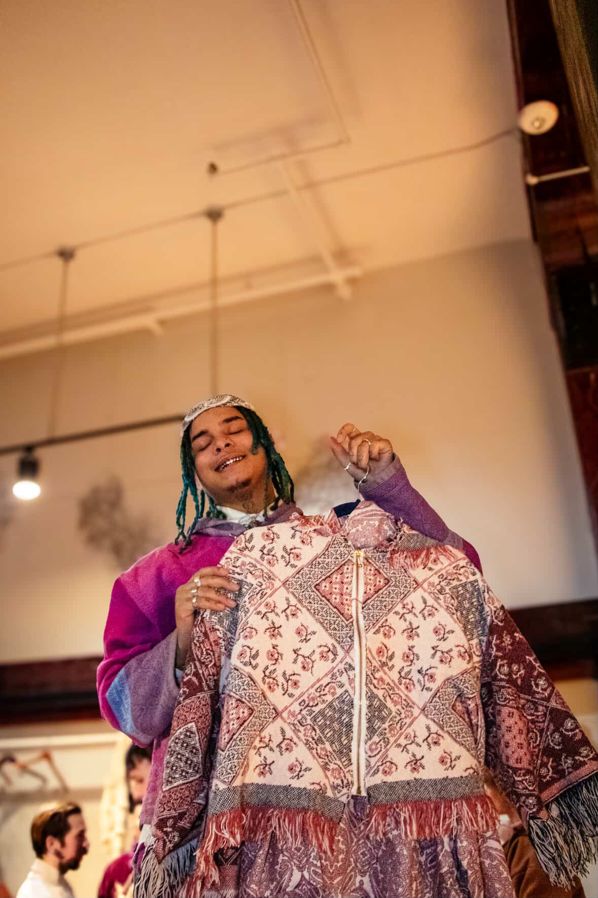 Person holding up a patterned garment beneath ceiling lights.