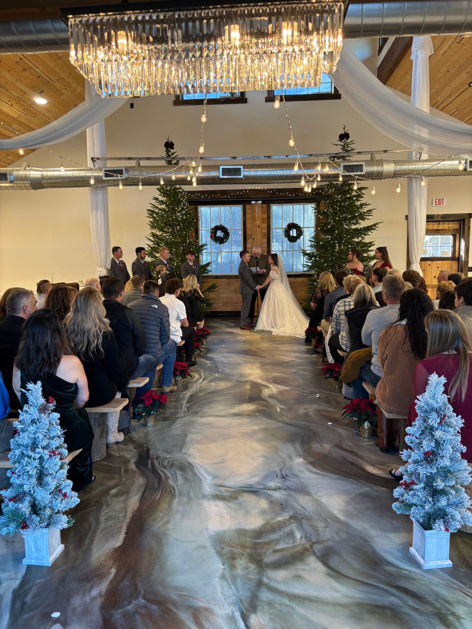 People gather around a long table beneath chandeliers, with blue floral arrangements and a polished stone floor.