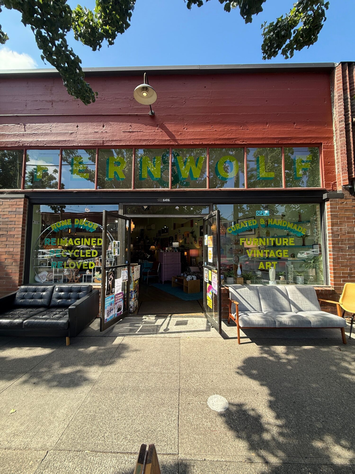A sidewalk-facing shop with a red awning, large windows, colorful signs, and outdoor display racks.