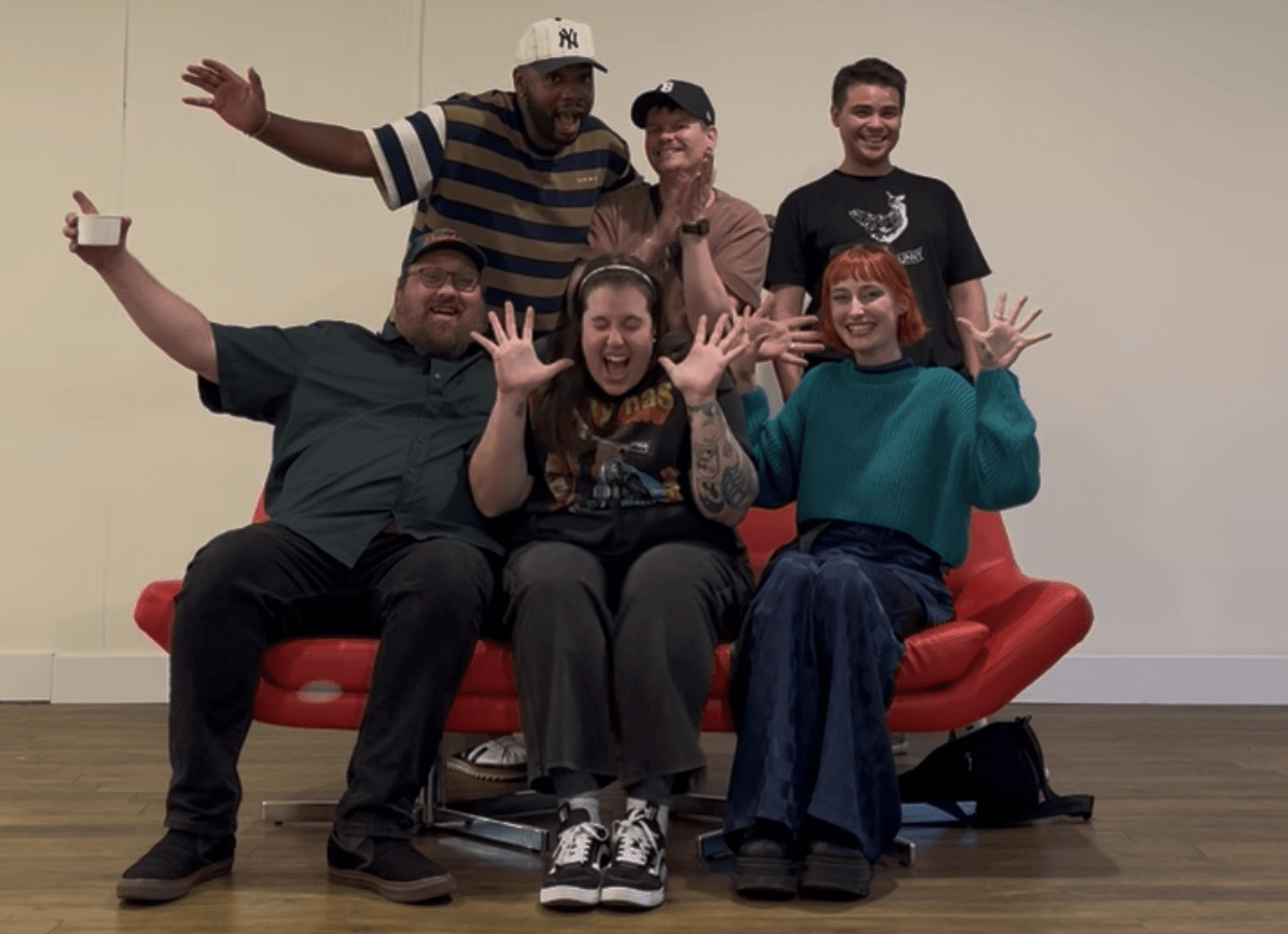 Six people pose together on a red couch in a gallery-like room.