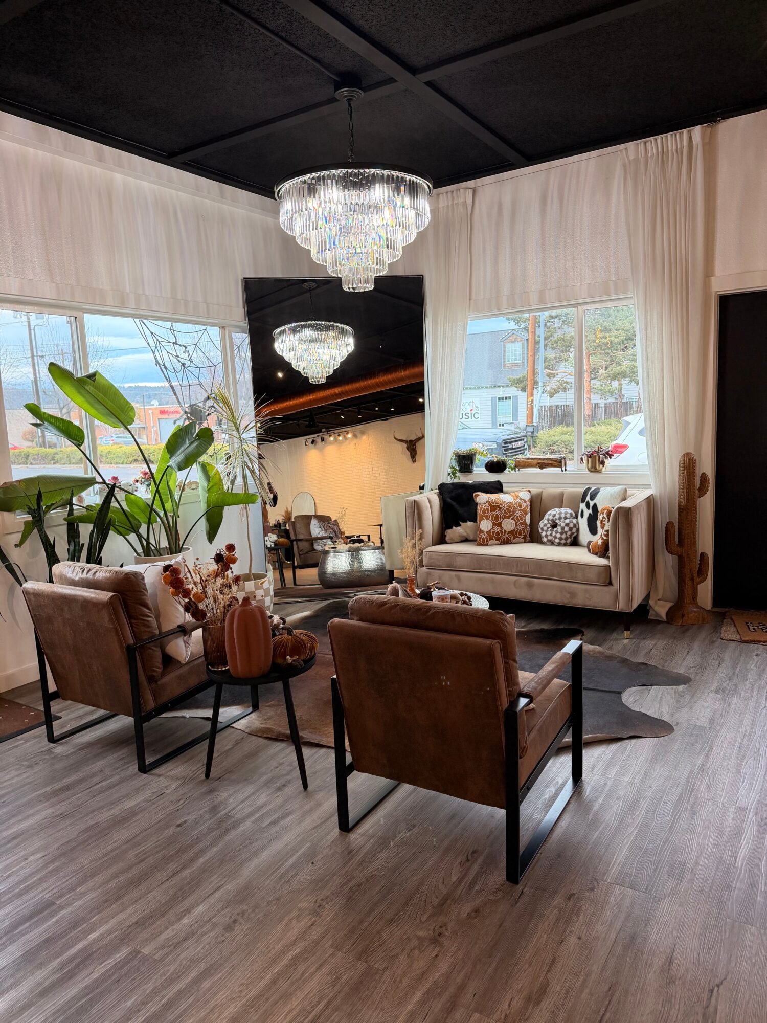 Living room with a chandelier, cream sofa, armchairs, plants, and large windows.